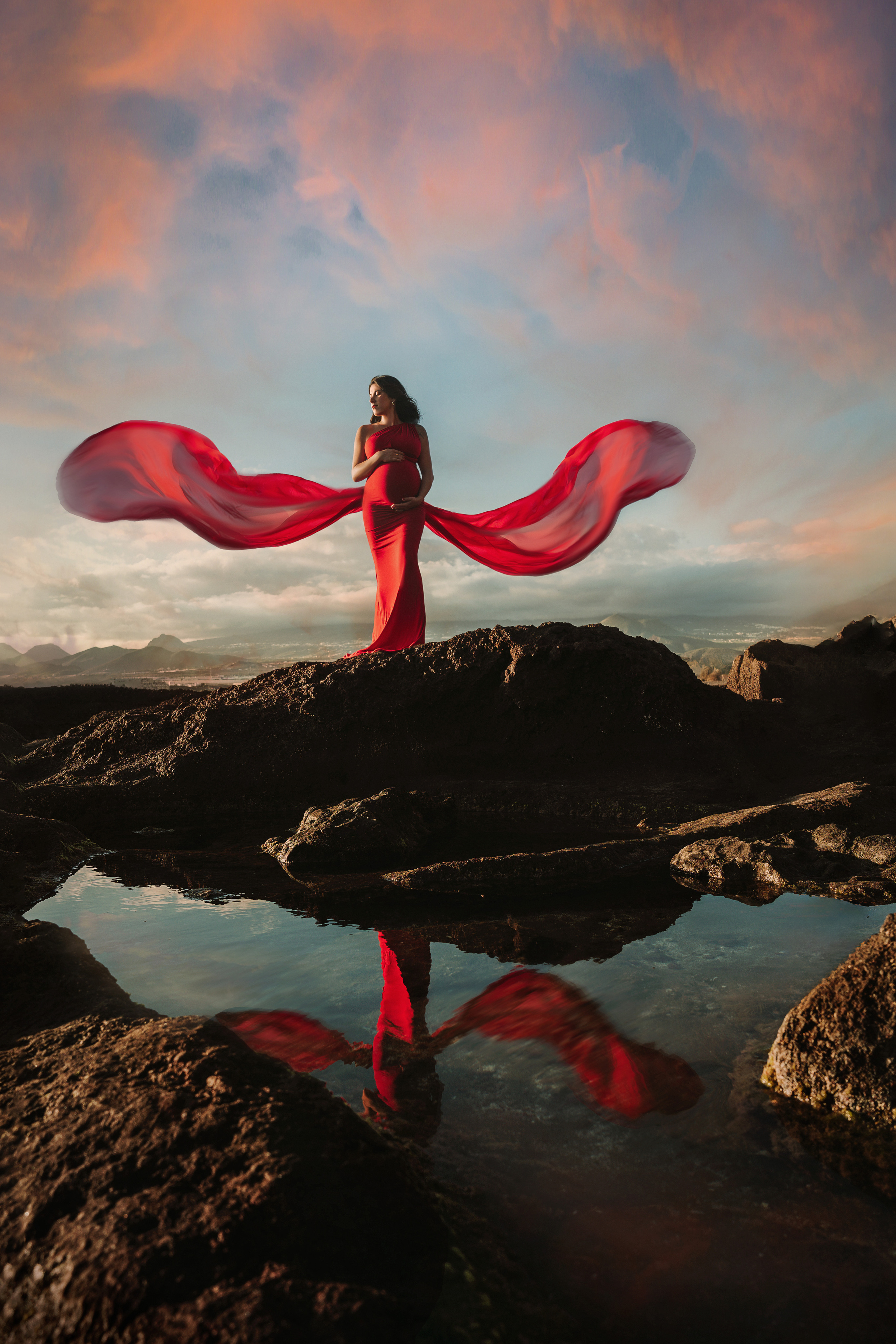 A pregnant girl in the flying red dress on a rock at the beach