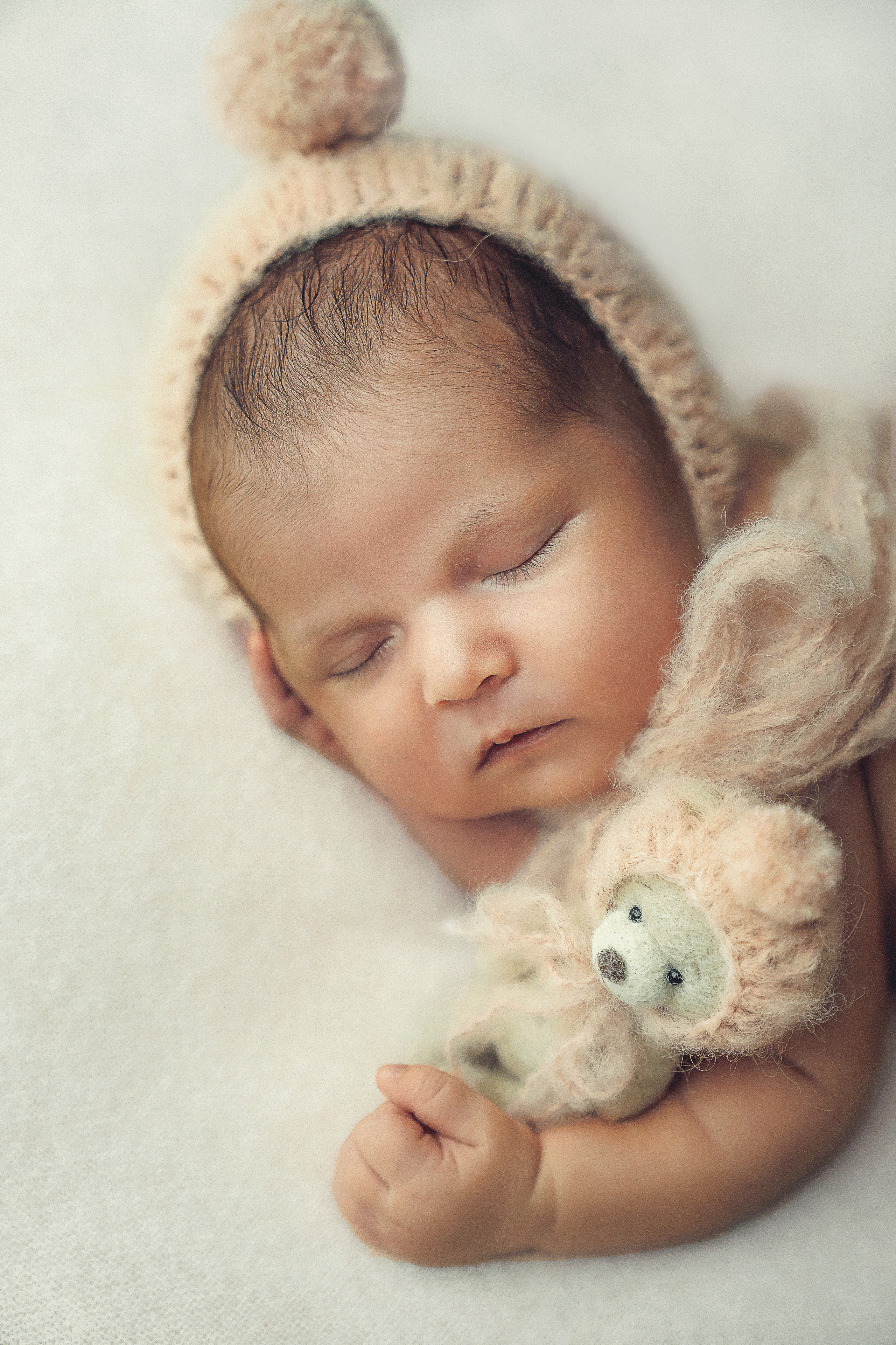 A newborn girl in a bonnet and a teddy bear in her hand