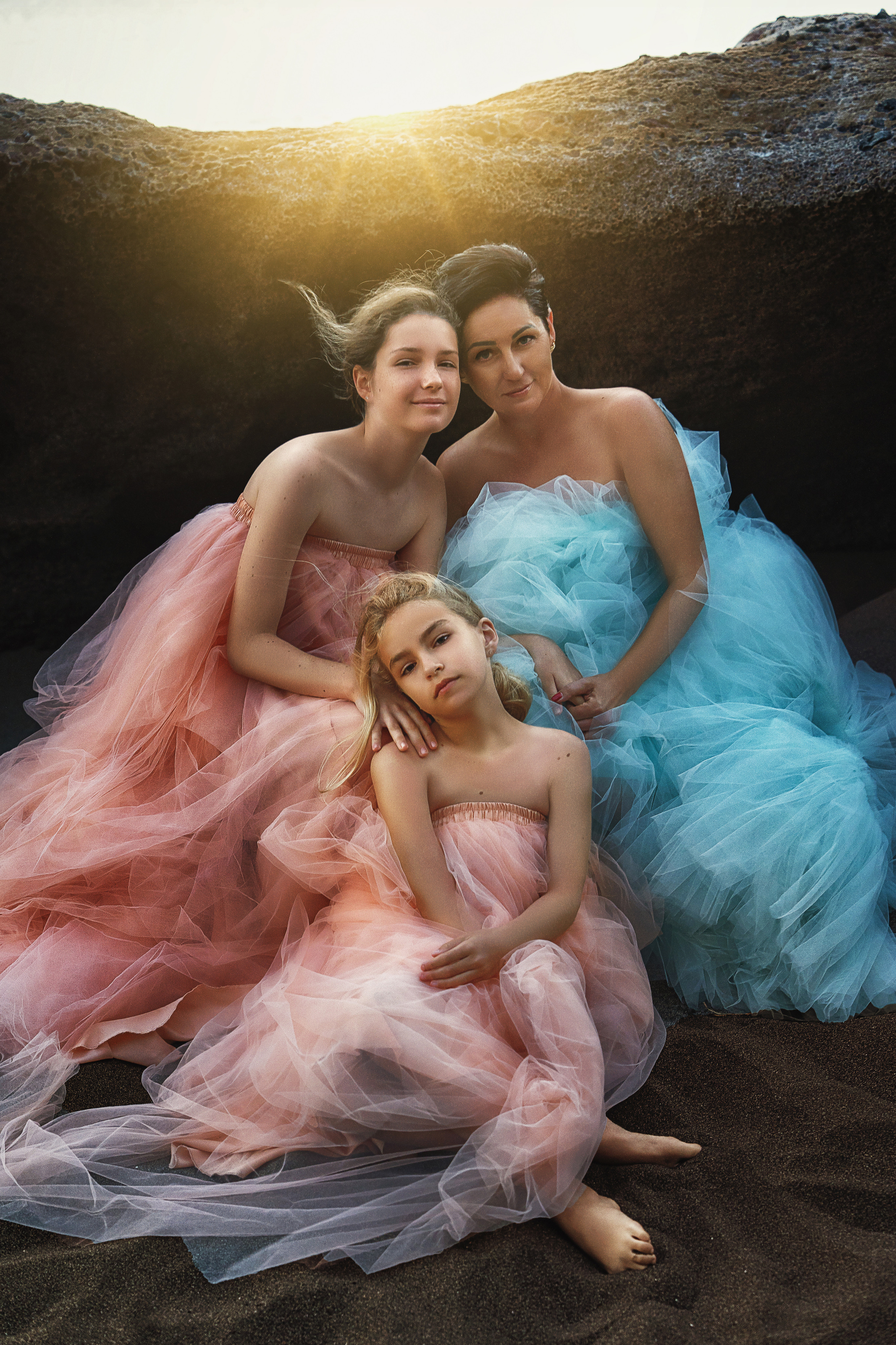 Mother with her daughters in tulle dresses on a rocky beach