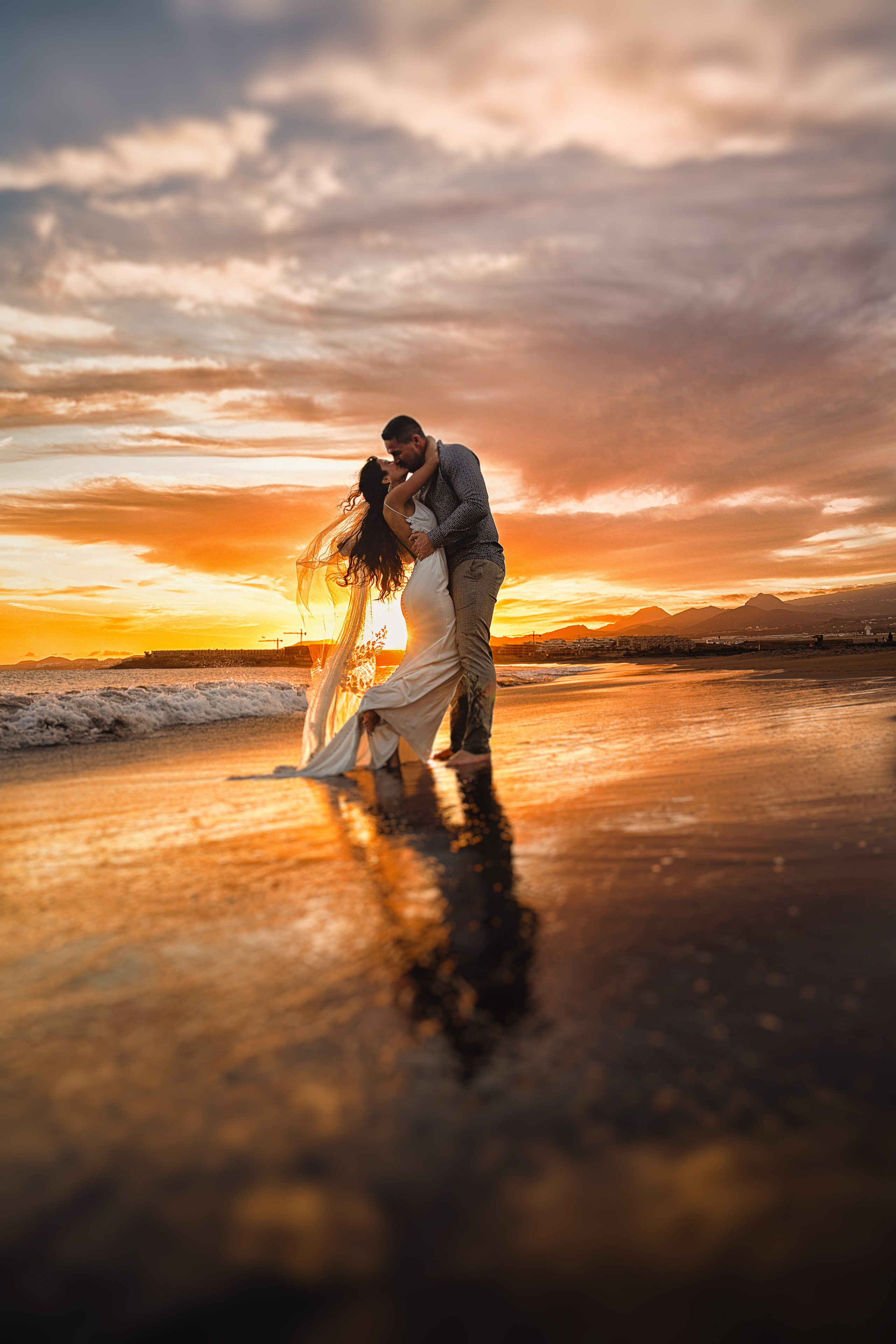 The bride and groom kissing on the beach at sunset