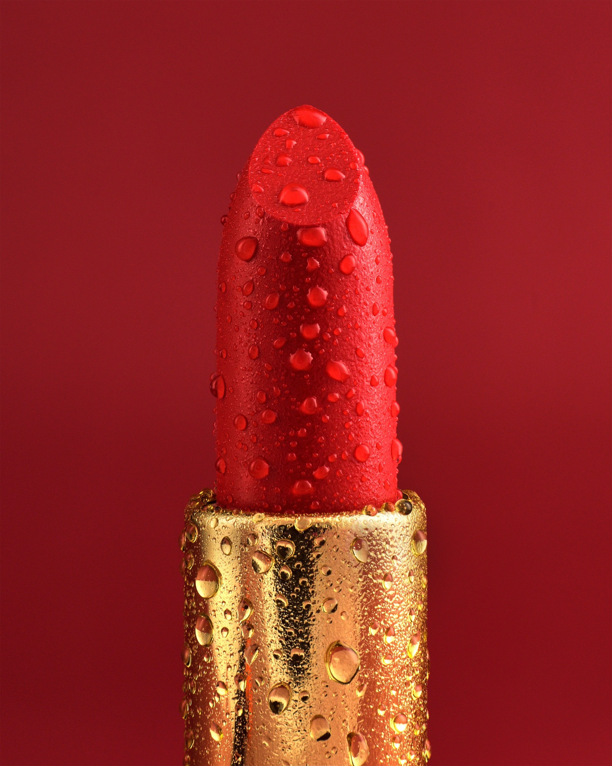 Close-up of a vibrant red lipstick with water droplets, in a gold case, set against a matching red background