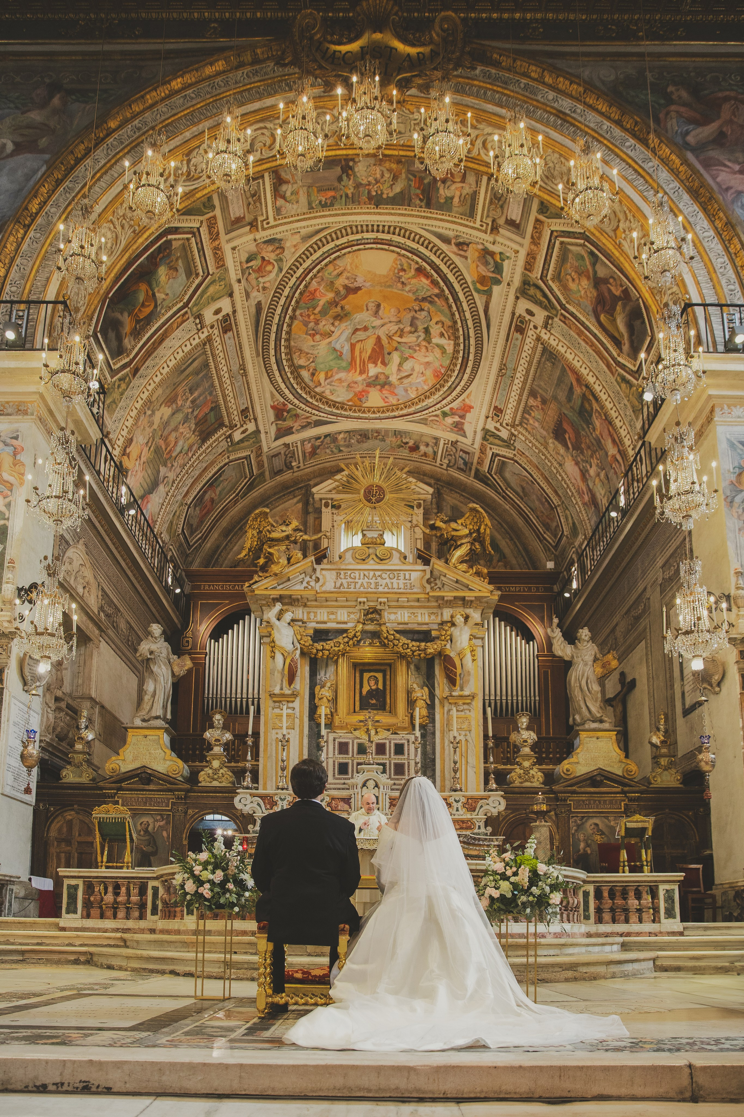 Couple at the altar in Santa Maria in Aracoeli, with chandeliers and a soft, romantic glow.