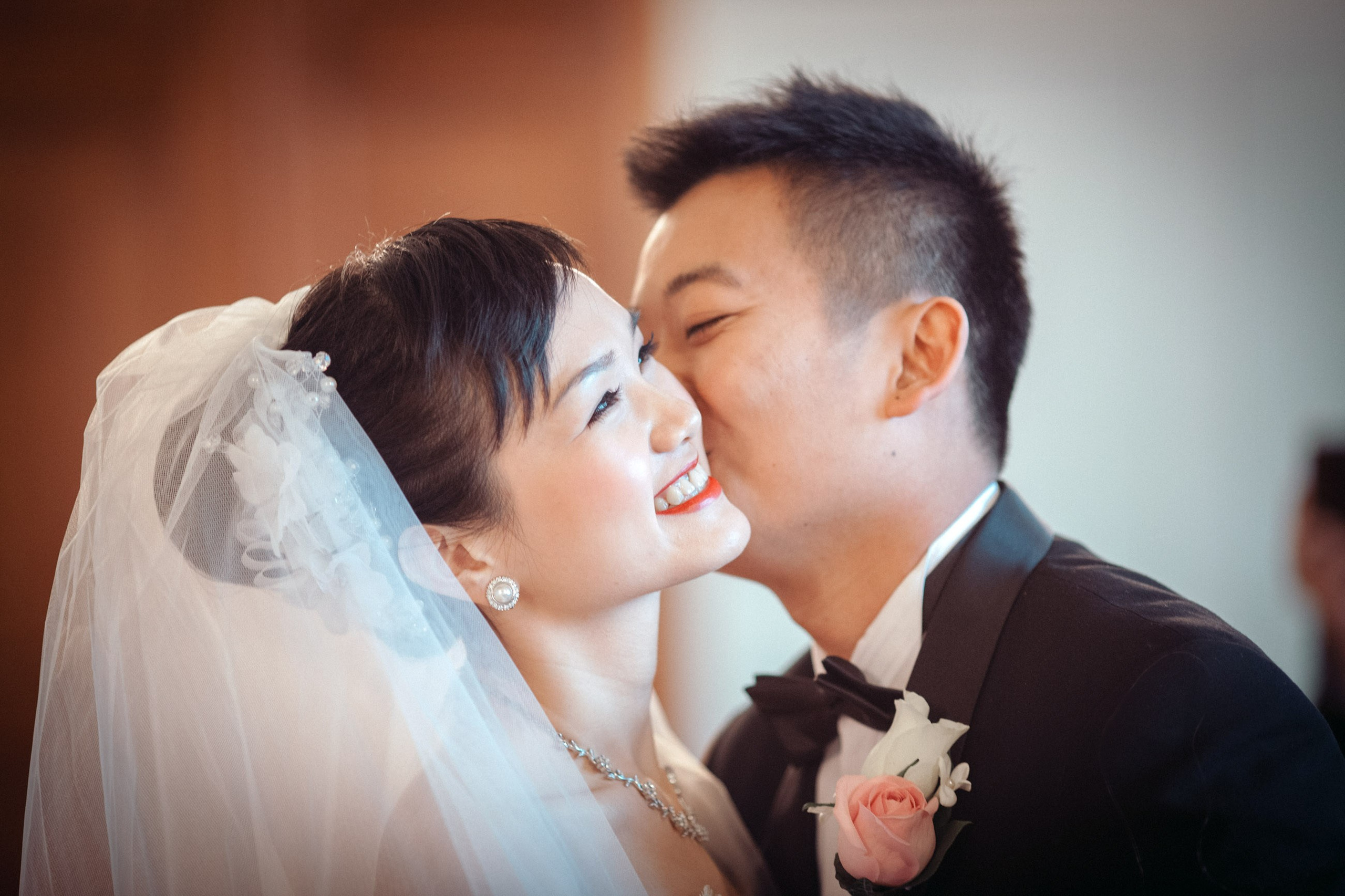 A smiling Hong Kong bride is kissed on the cheek by her groom during their candlelit wedding ceremony at the Castle Hluboka in the Czech Republic.
