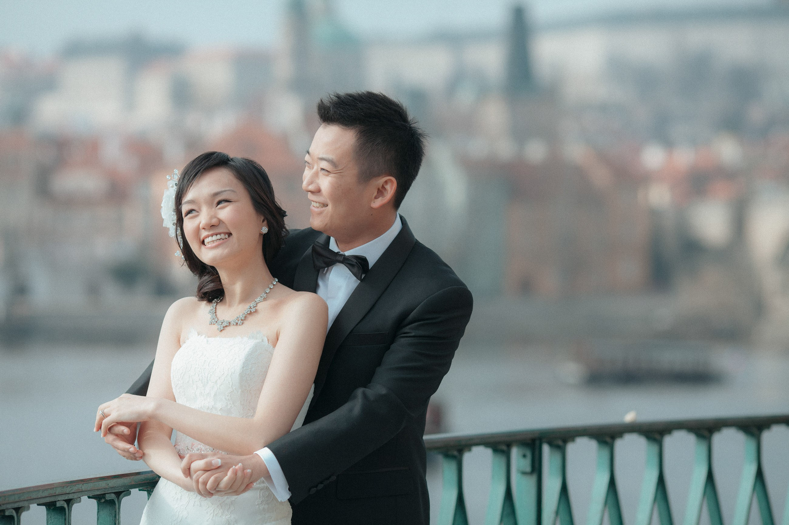With the city of Prague behind them, a young, elegant bride & groom from Hong Kong snuggle up for a photo during their Love Story photo session.