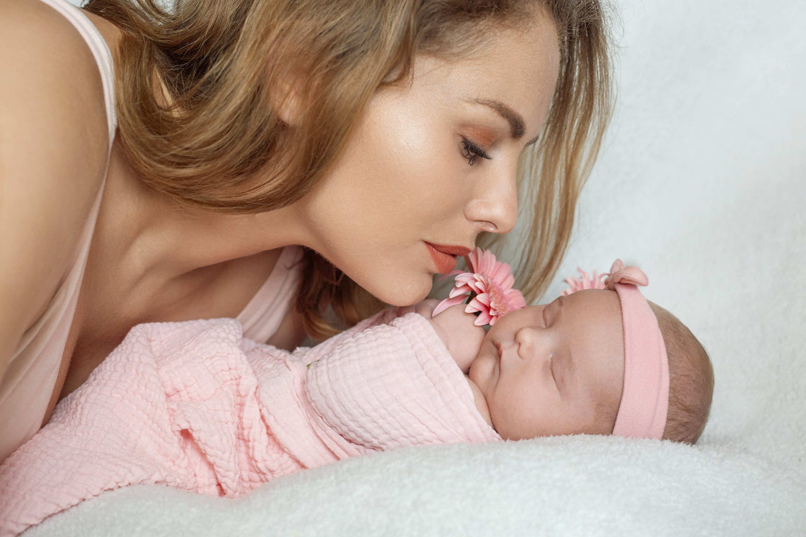 Maman embrassant tendrement son nouveau-né emmailloté en rose, séance photo naissance douce et intime