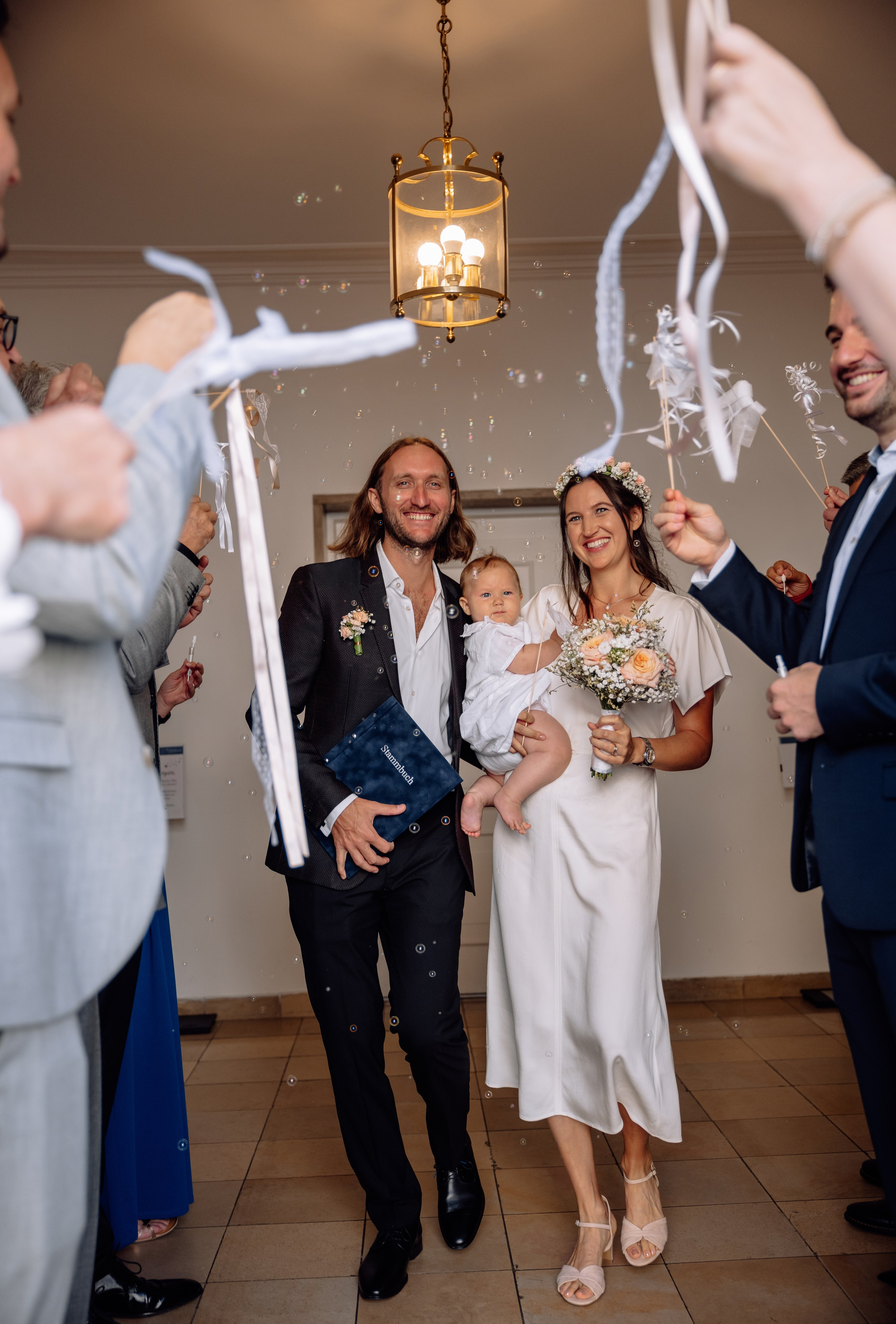 Glückliche Eltern und Baby verlassen Standesamt Mandlstraße 14 – weiße Bänder in der Luft