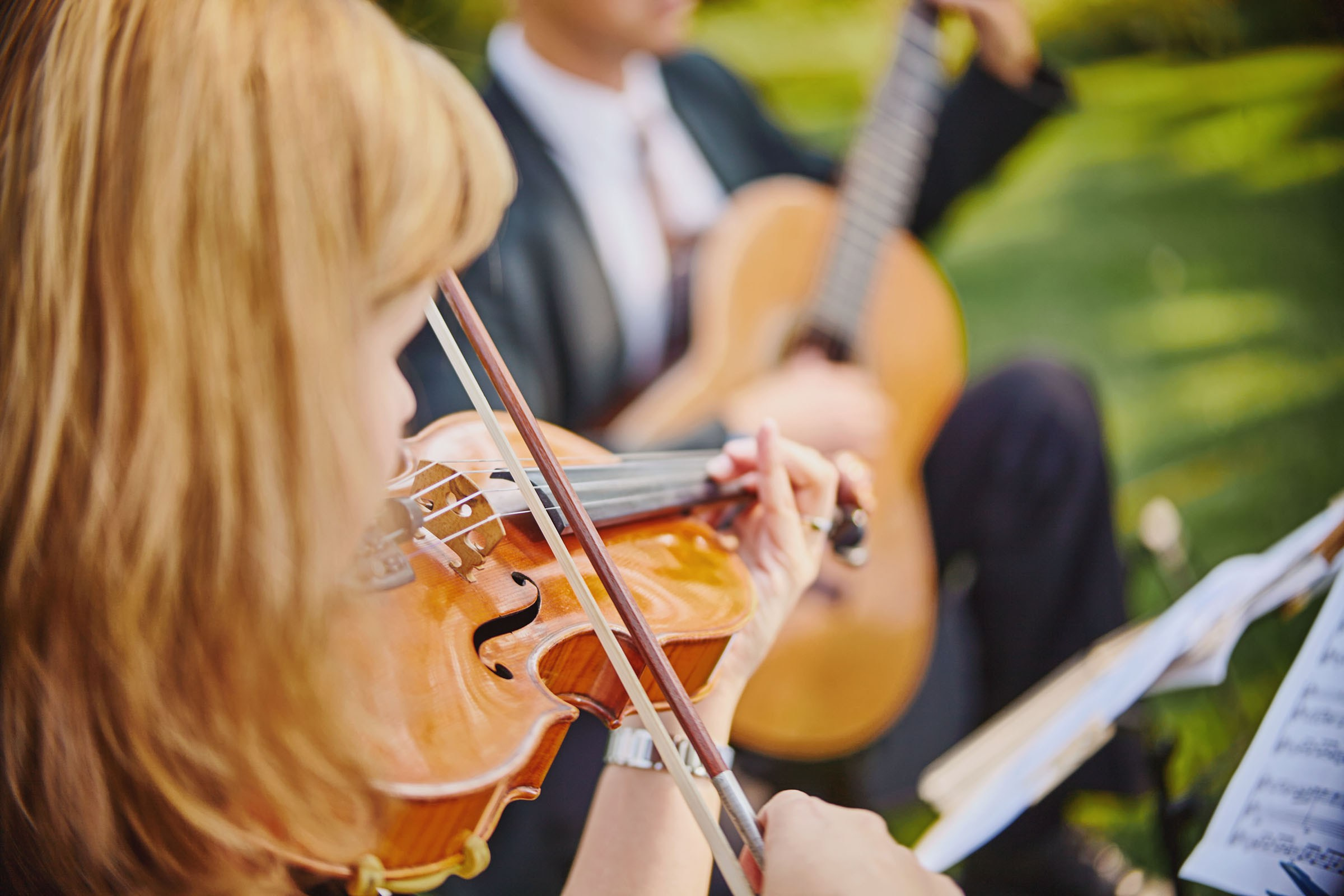 Violinist warming up in garden for outdoor wedding ceremony.