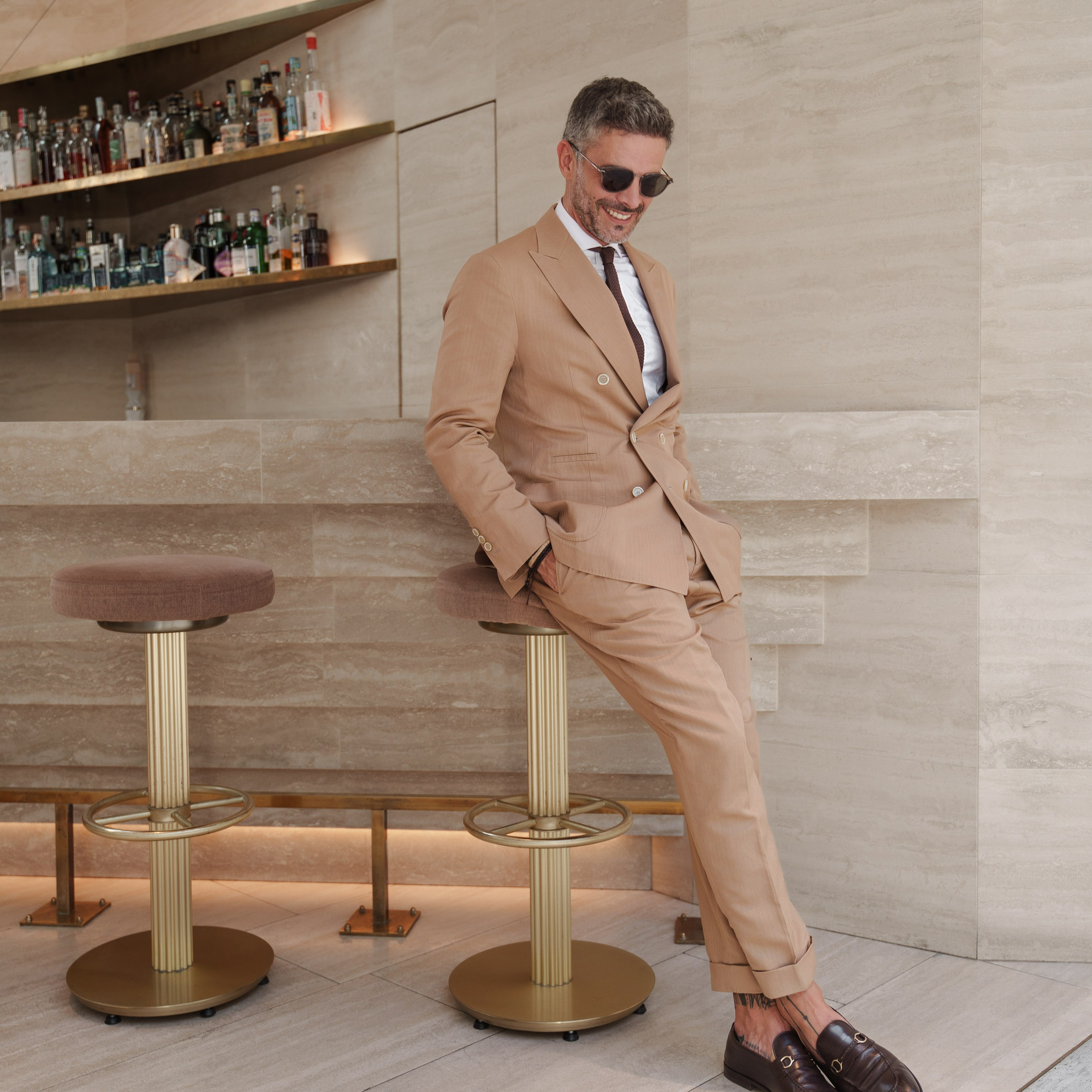 Relaxed businessman in a beige suit leaning against a stylish bar counter with a modern minimalist design