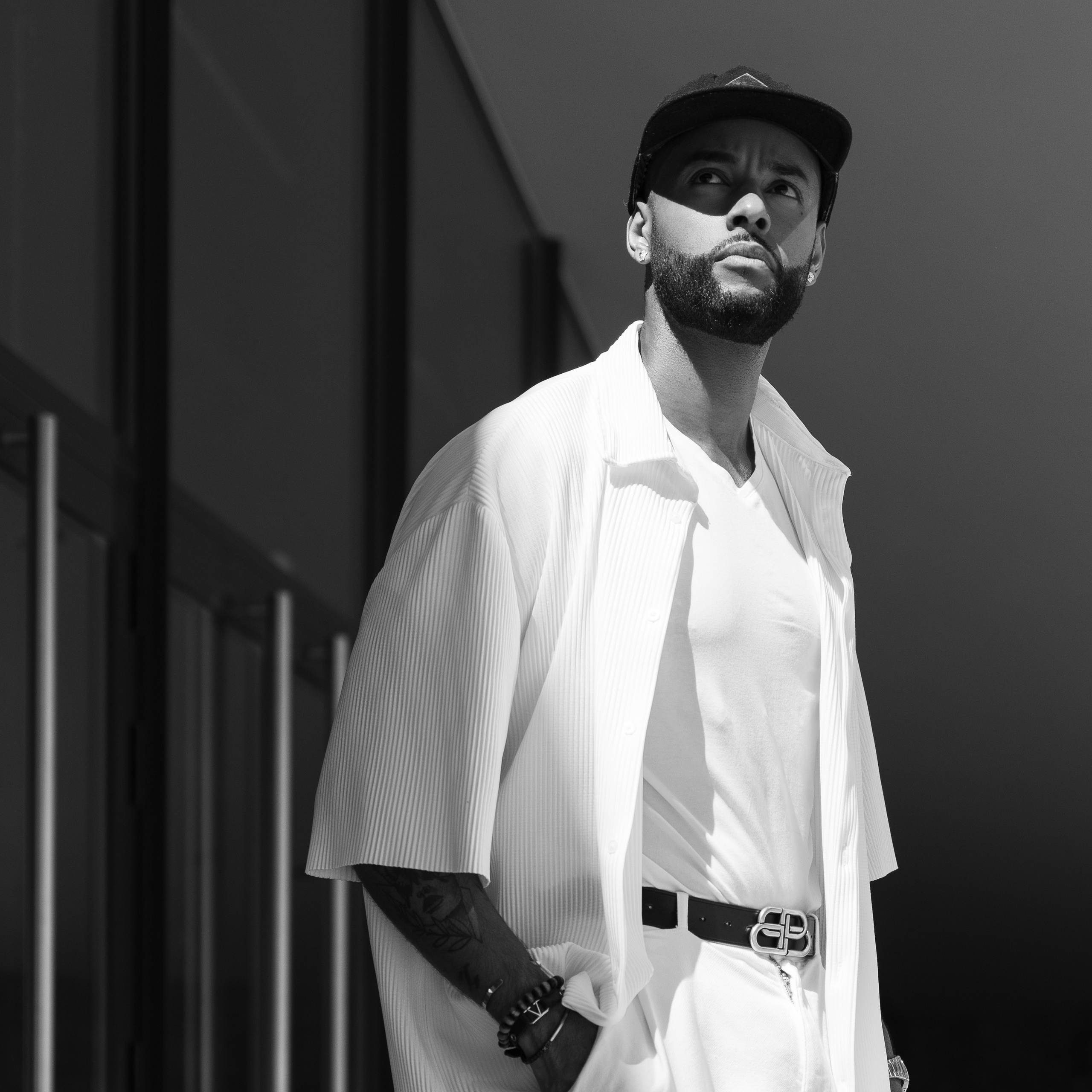 Monochrome portrait of a man in a white outfit and cap, standing confidently in sunlight