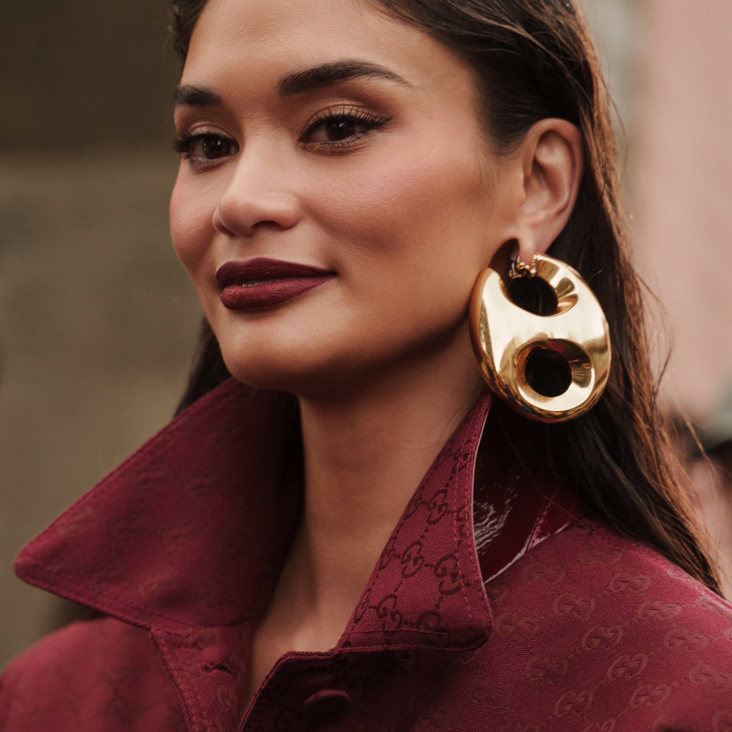Pia Wurtzbach in a designer maroon jacket and statement gold earring at Milan Fashion Week captured by a photographer in Milan