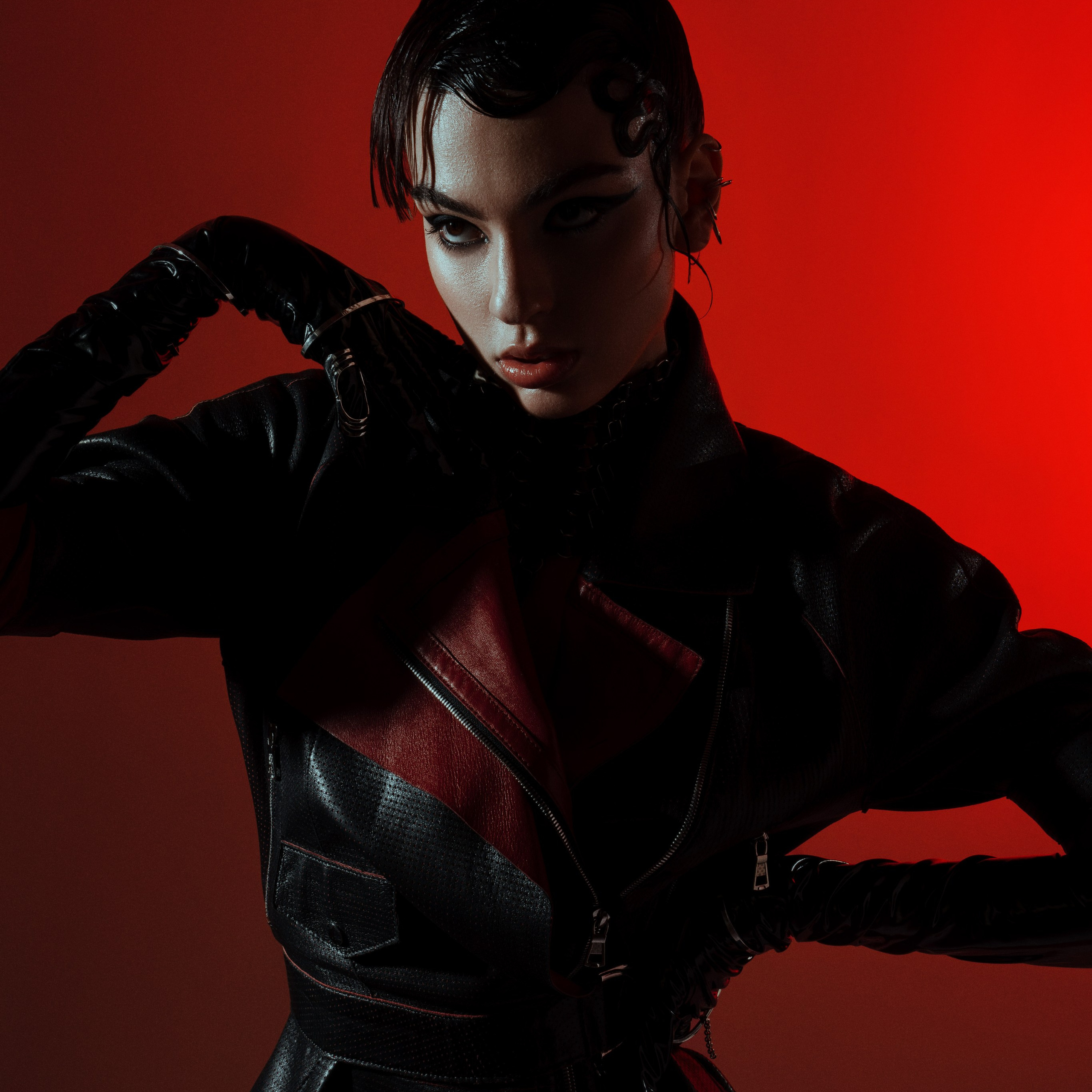 High-fashion editorial portrait of a woman in a black and red leather outfit, dramatic lighting against a bold red background