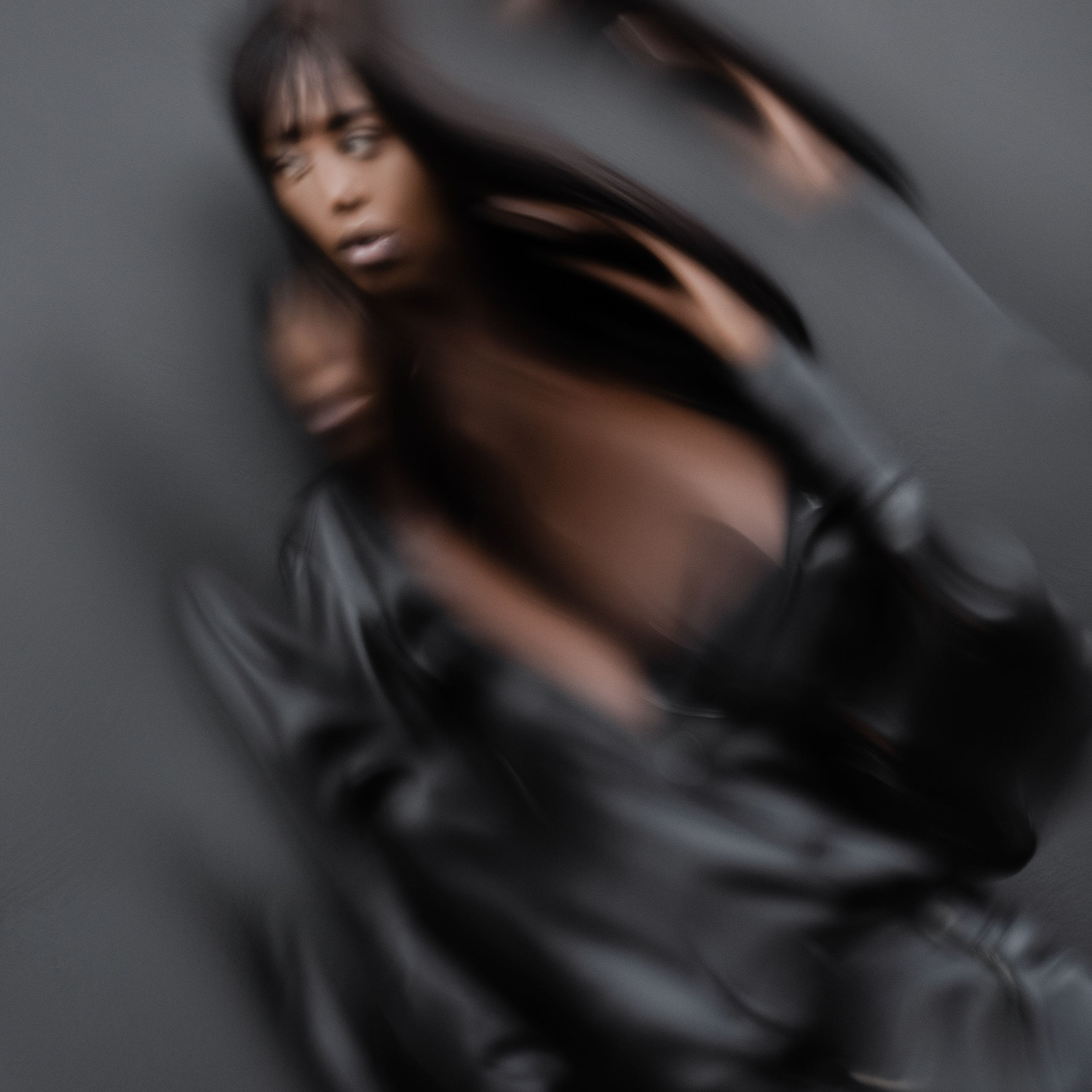 Creative motion blur effect of a woman in black leather attire against a grey backdrop