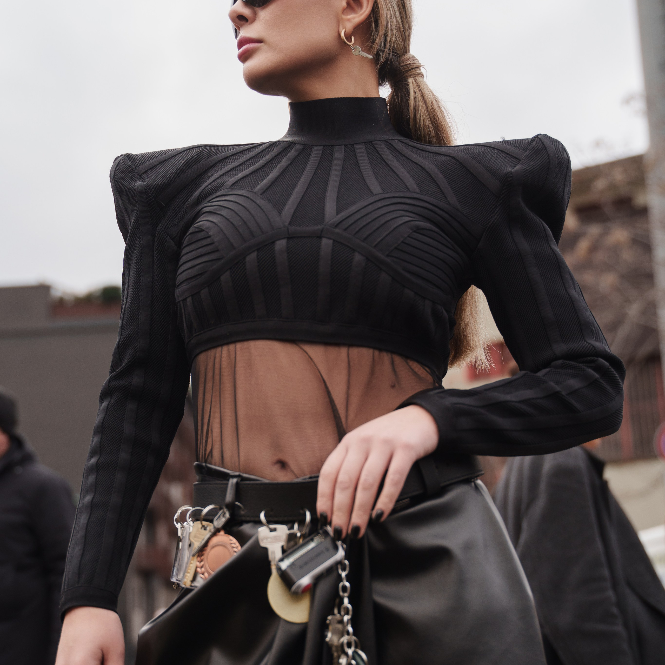 Fashion-forward woman in a sheer-panel black top and leather skirt with statement accessories