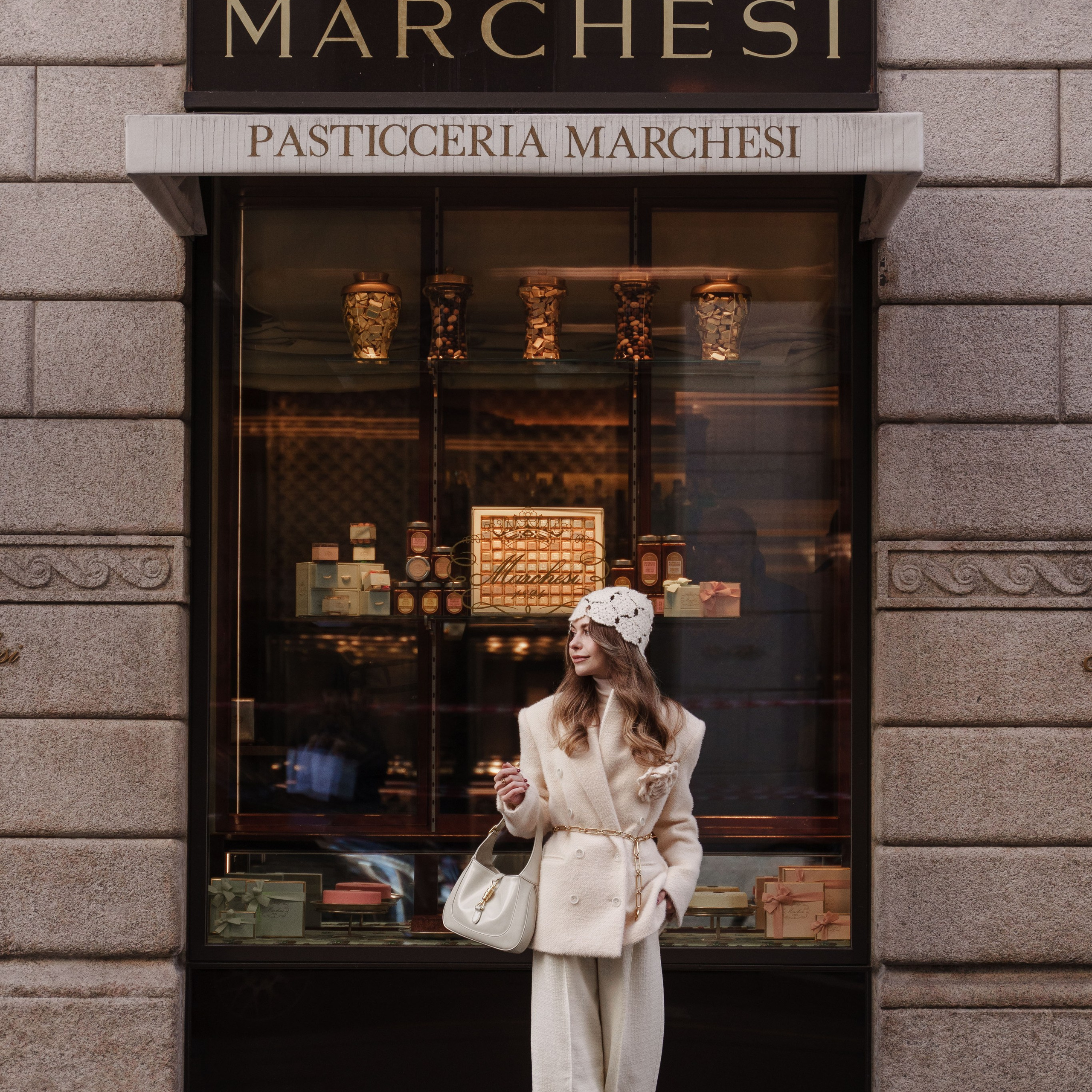 Luxury street style photoshoot of a woman in a white wool coat, standing in front of the Pasticceria Marchesi in Milan. Fashion editorial, personal branding photography.