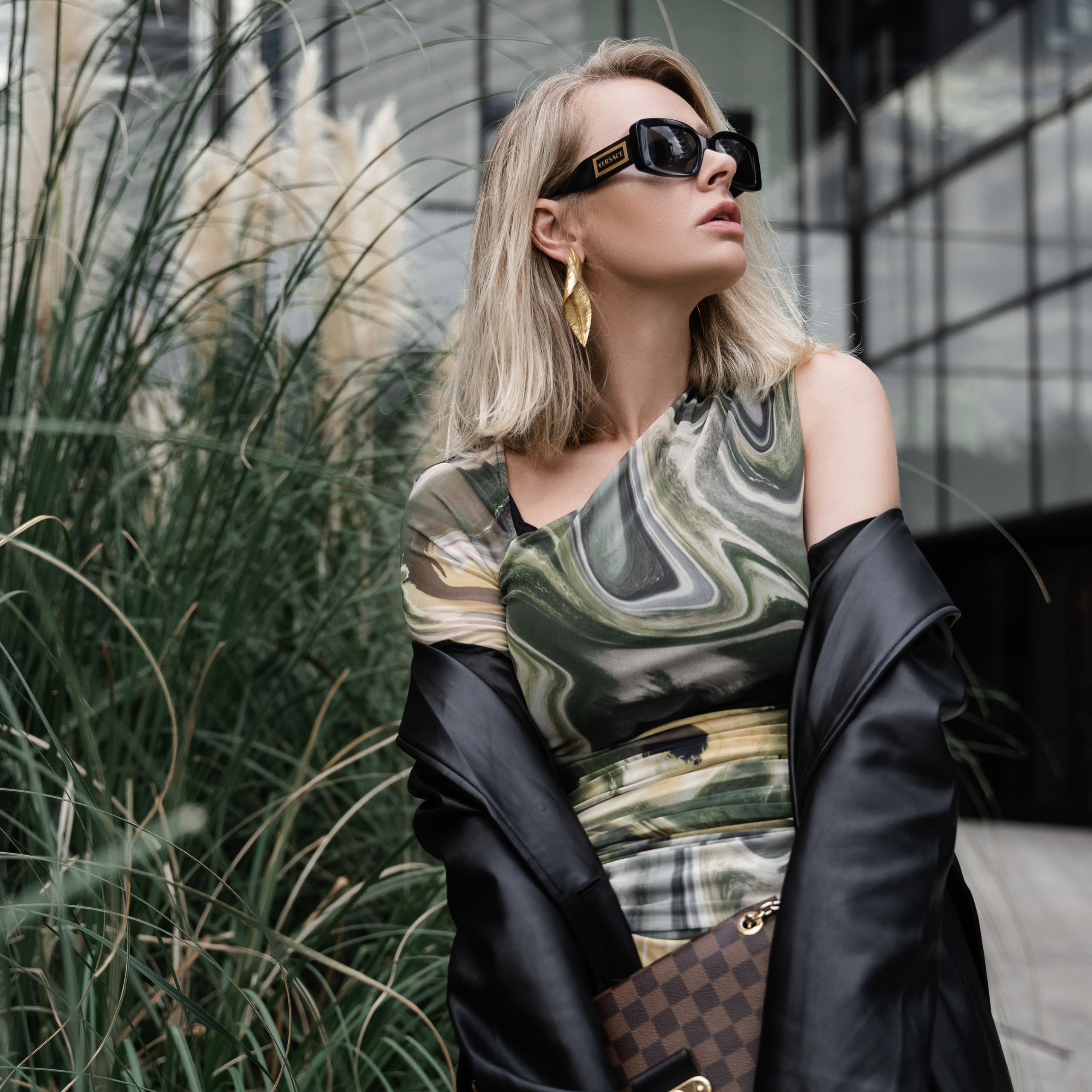 Stylish woman in a flowing dress and fencing mask stands on rocks by the sea, holding a fencing foil.