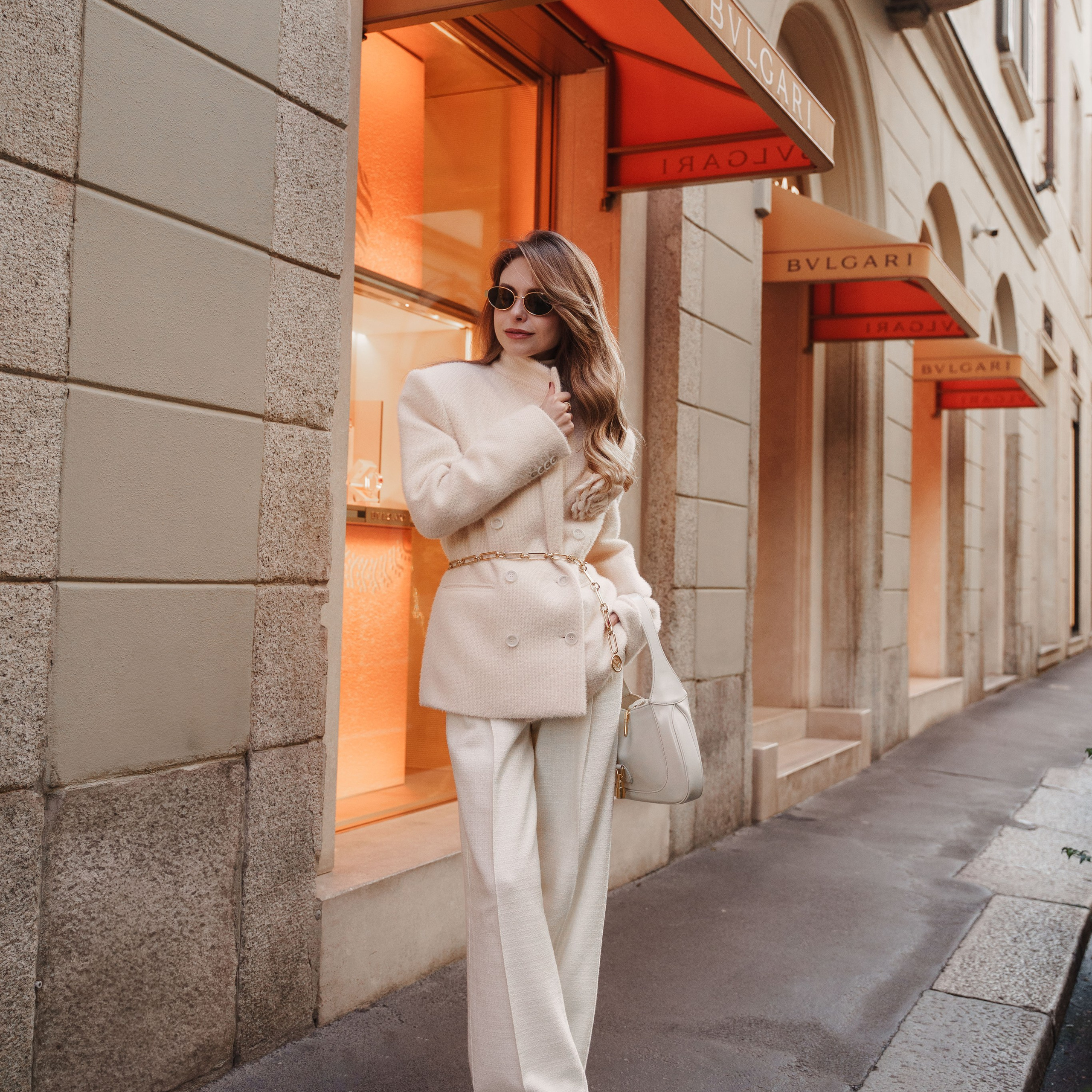 Elegant woman in a white suit walking past the BVLGARI boutique in Milan, exuding luxury and sophistication