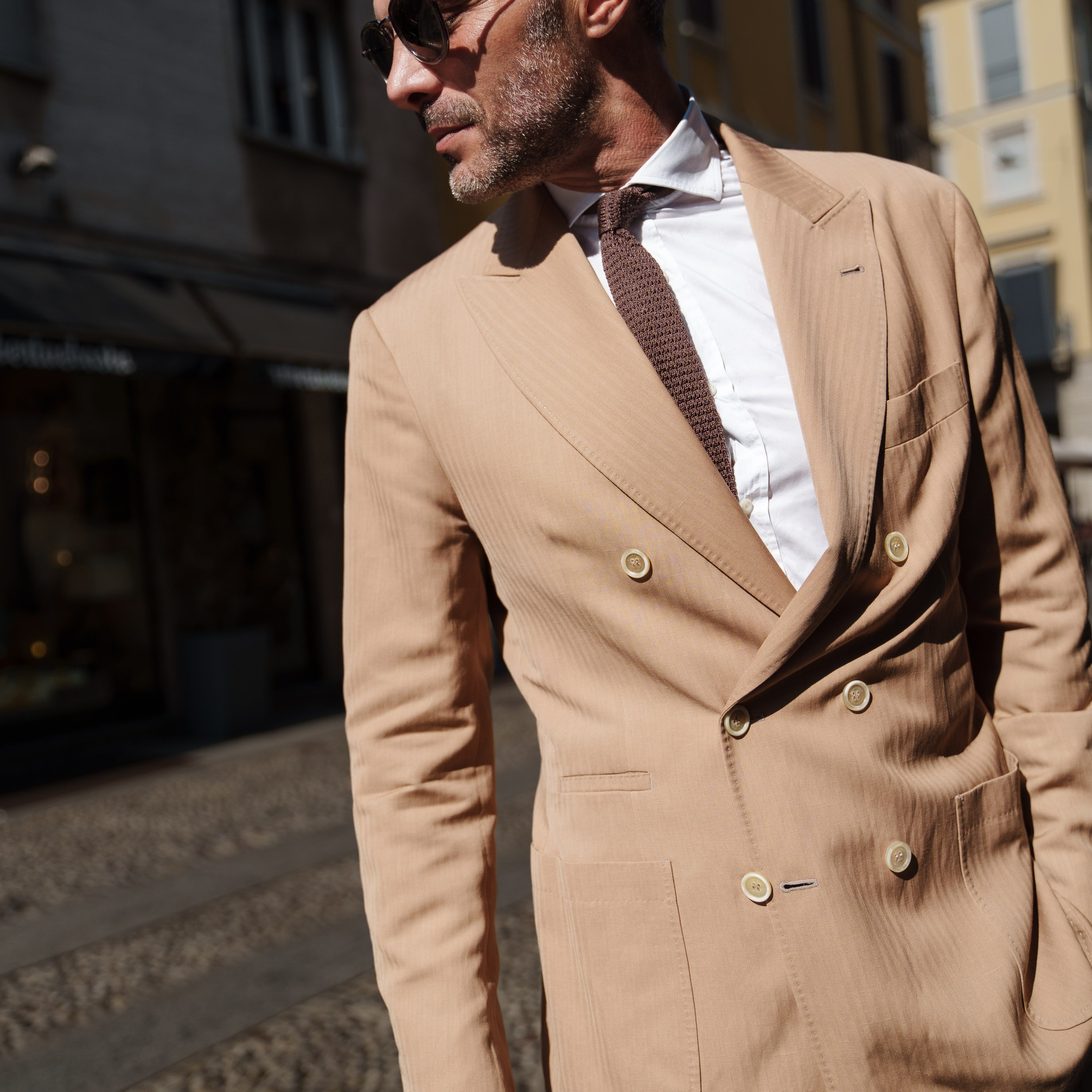 Fashion-forward man in a beige suit and sunglasses, captured under bright Milanese sunlight with a confident expression