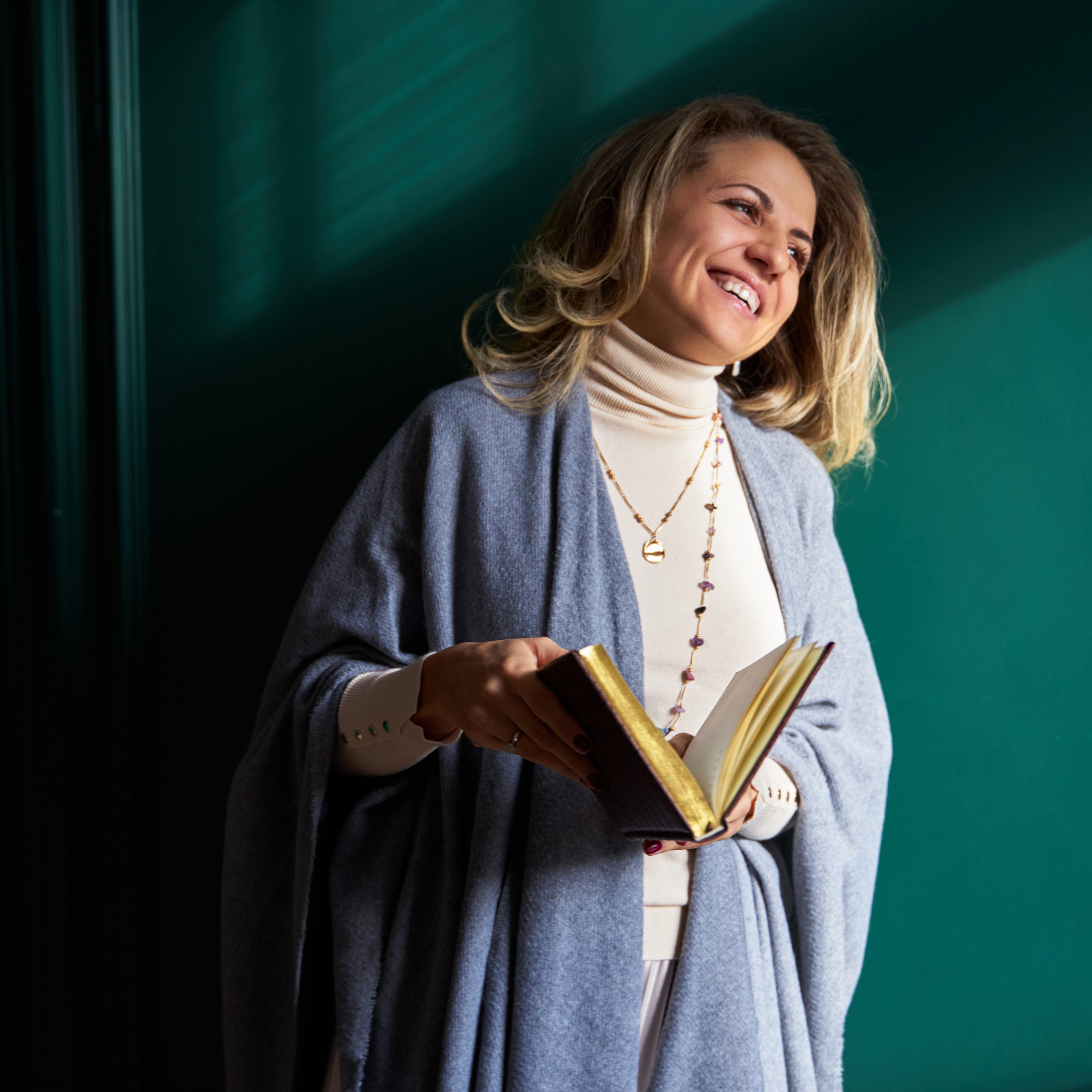 Joyful woman in a blue cardigan and white turtleneck holding an open book