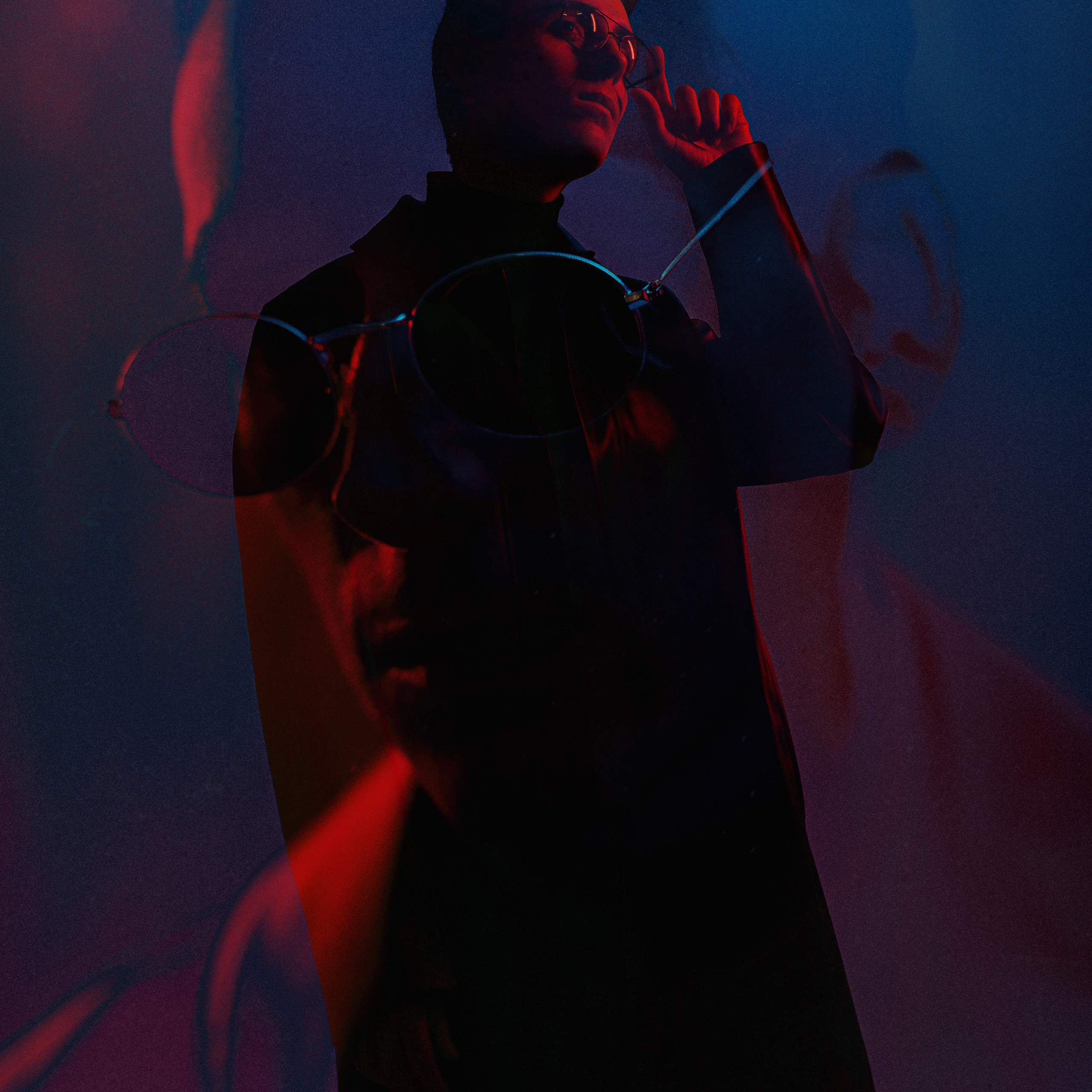 Mysterious silhouette of a person in dark attire with sunglasses, highlighted with purple and red lighting