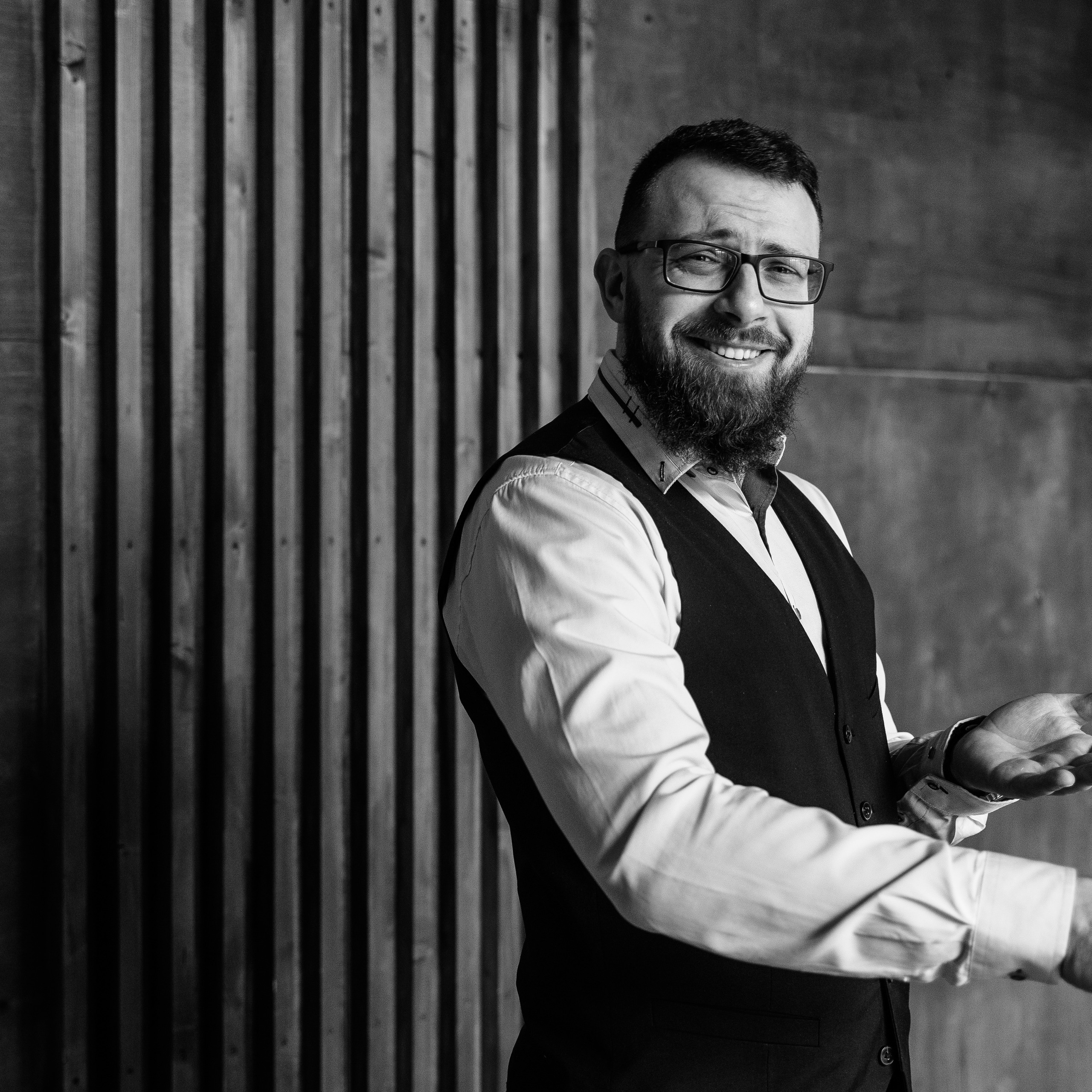 Monochrome image of a bearded man in a waistcoat gesturing with hands as if in conversation
