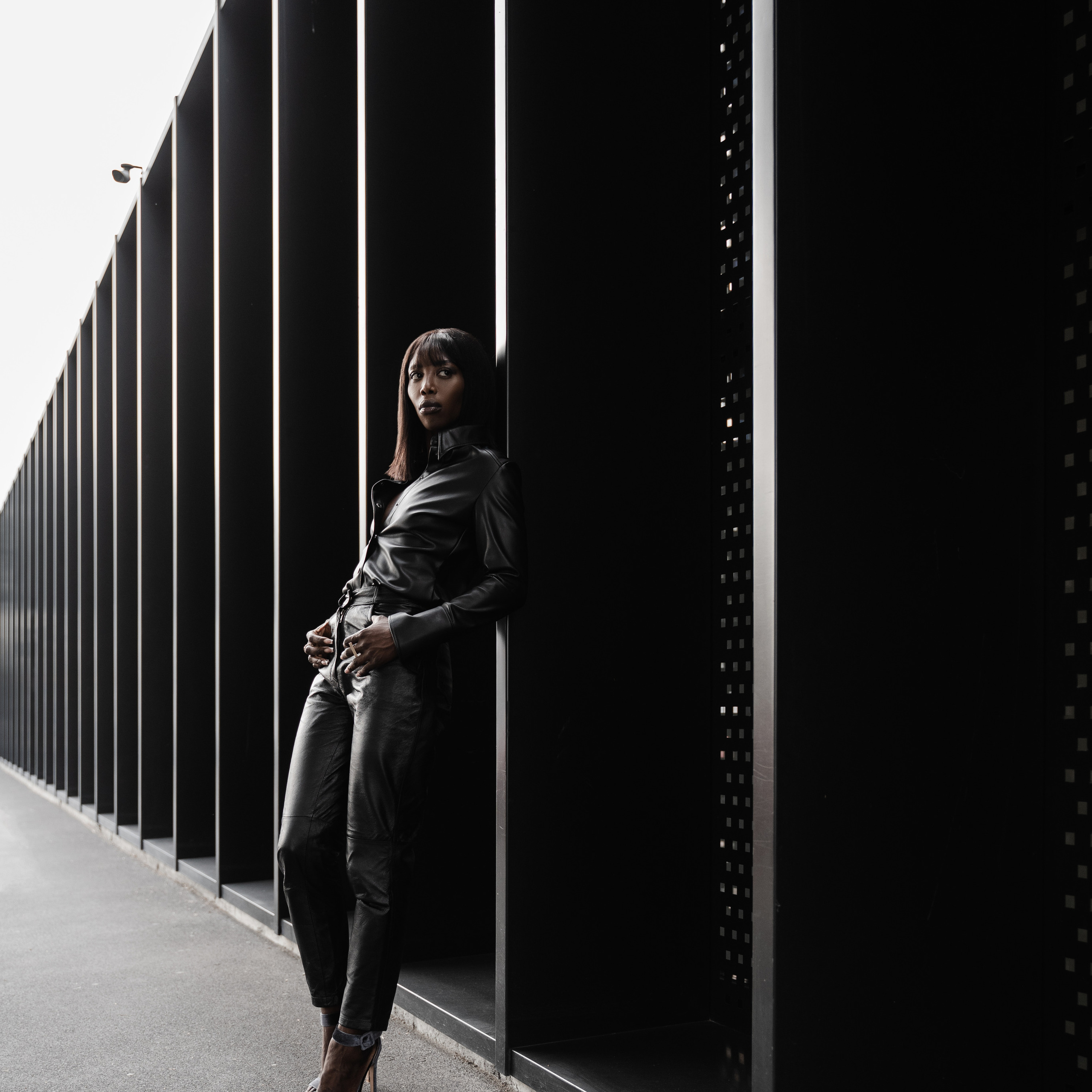 Woman in chic attire leaning against a modern black wall