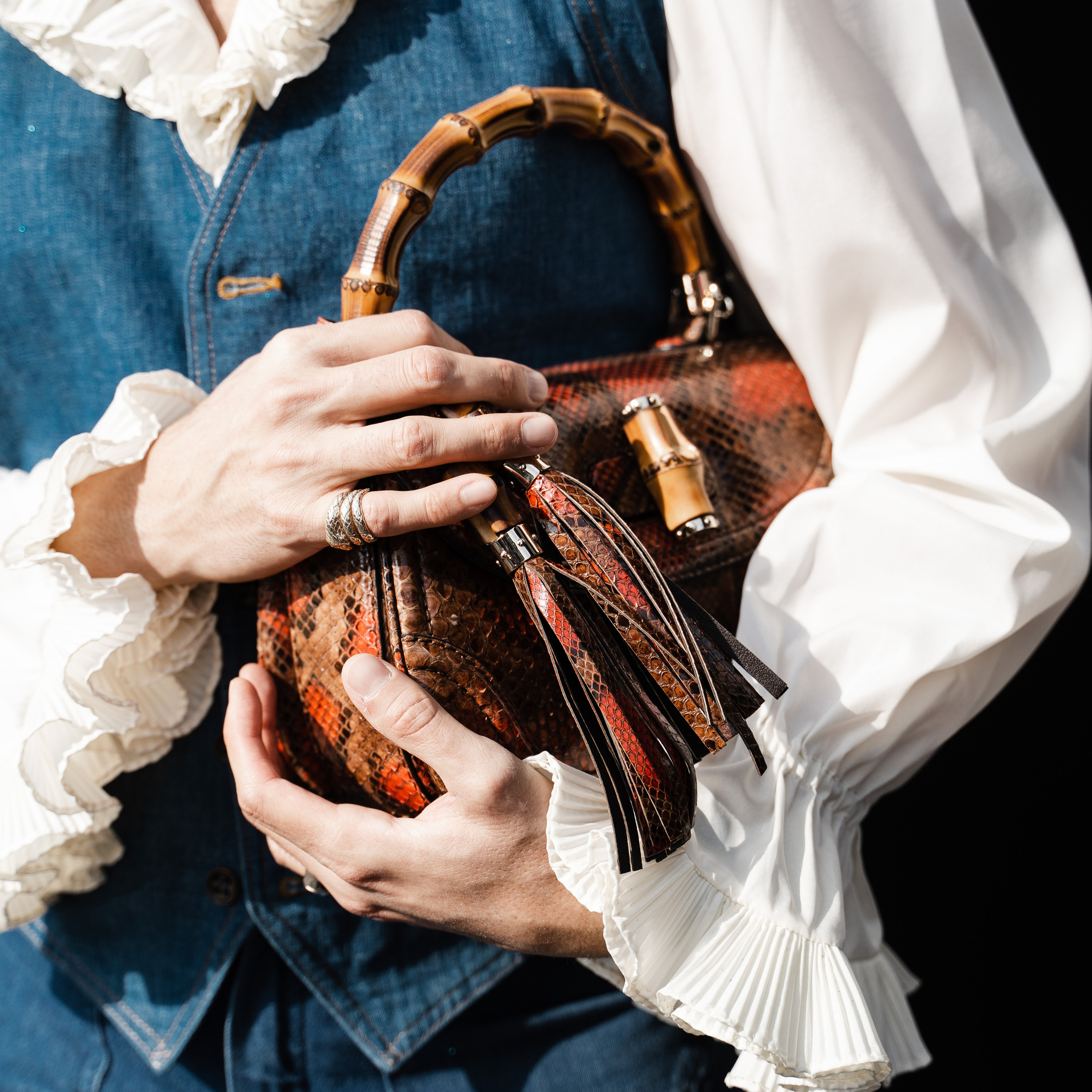 Close-up of a man’s hands adorned with rings, holding a designer python leather handbag