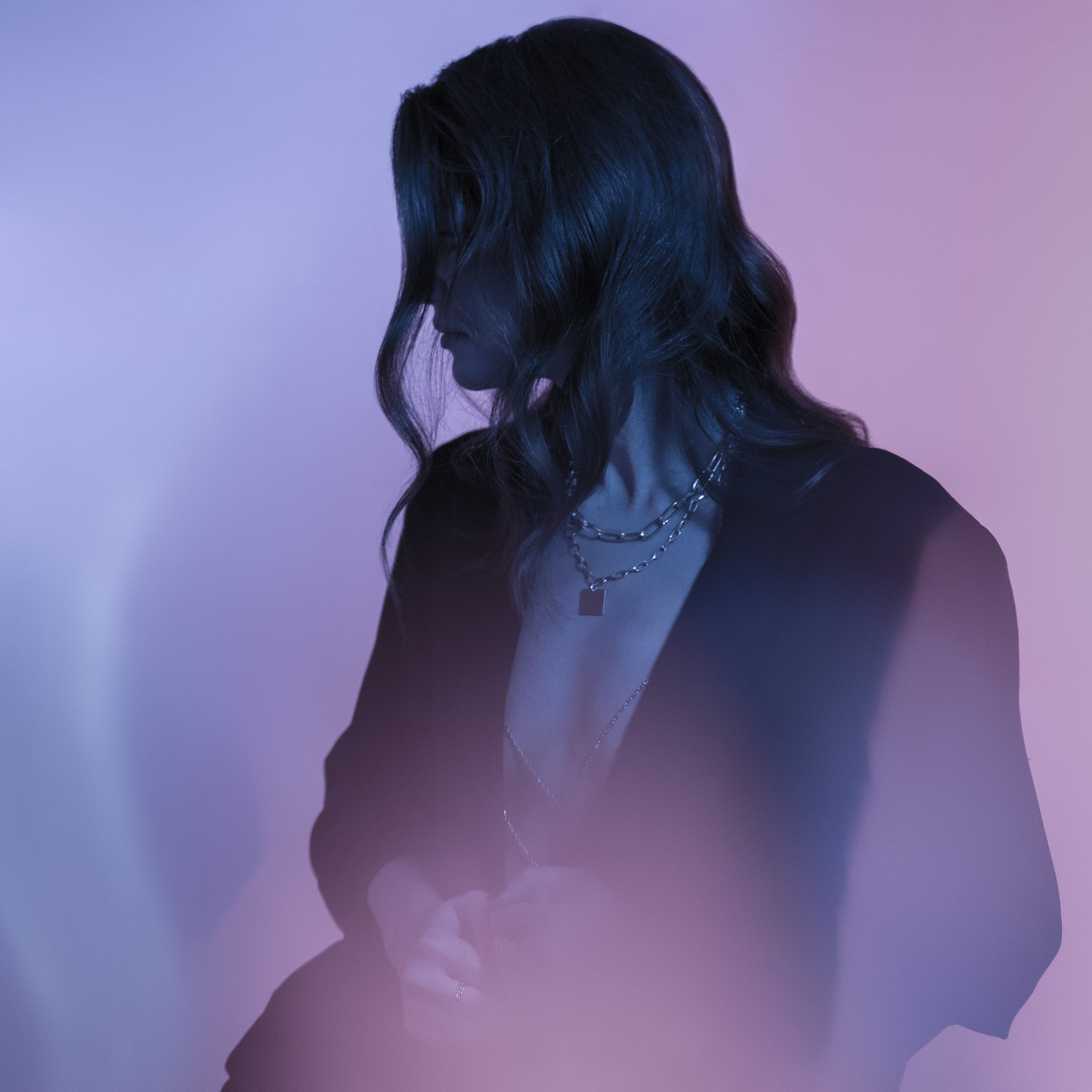 Elegant woman in black blazer covering her mouth with hands against an orange gradient background.