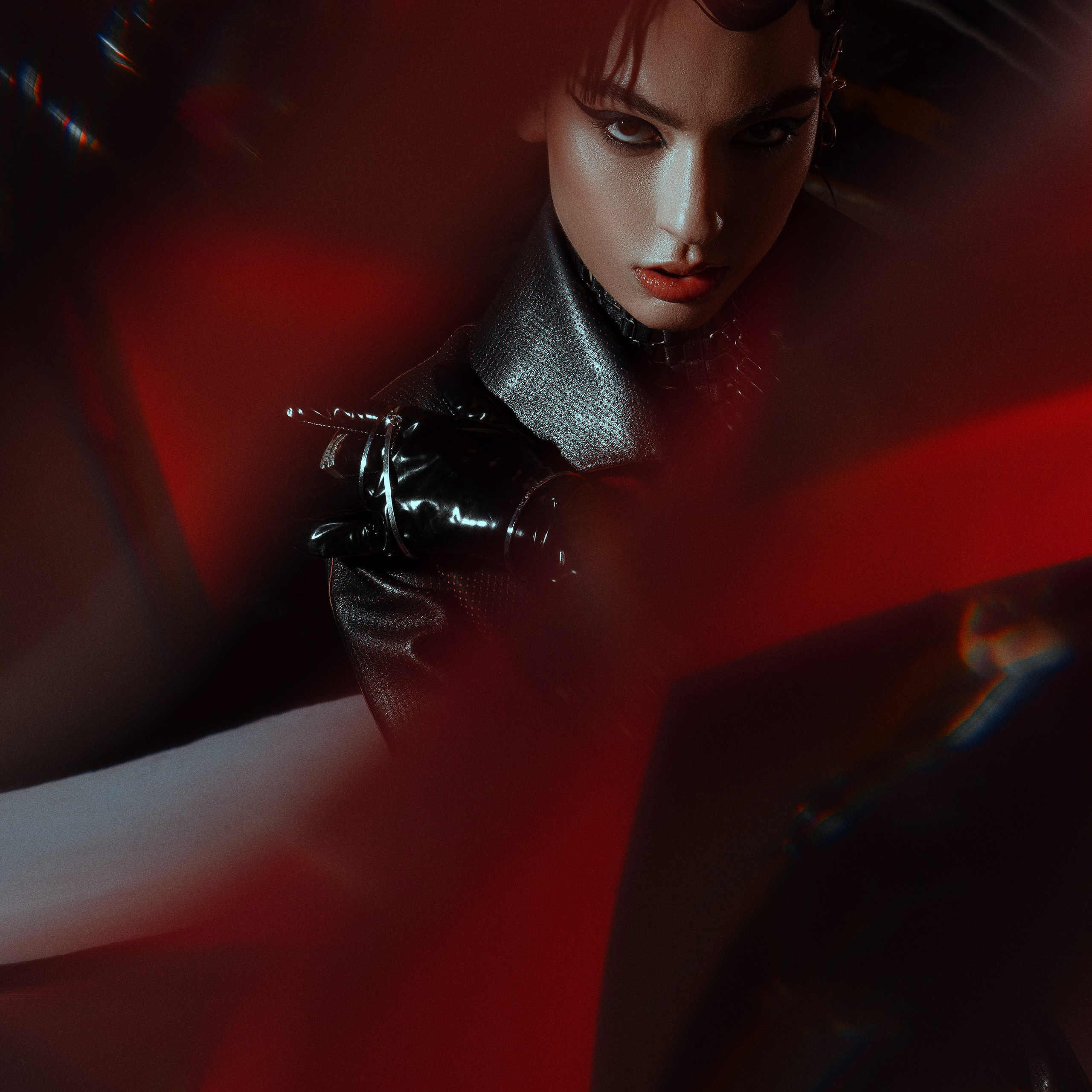 Fashion model in a black leather jacket with striking makeup, intense gaze through a red abstract foreground