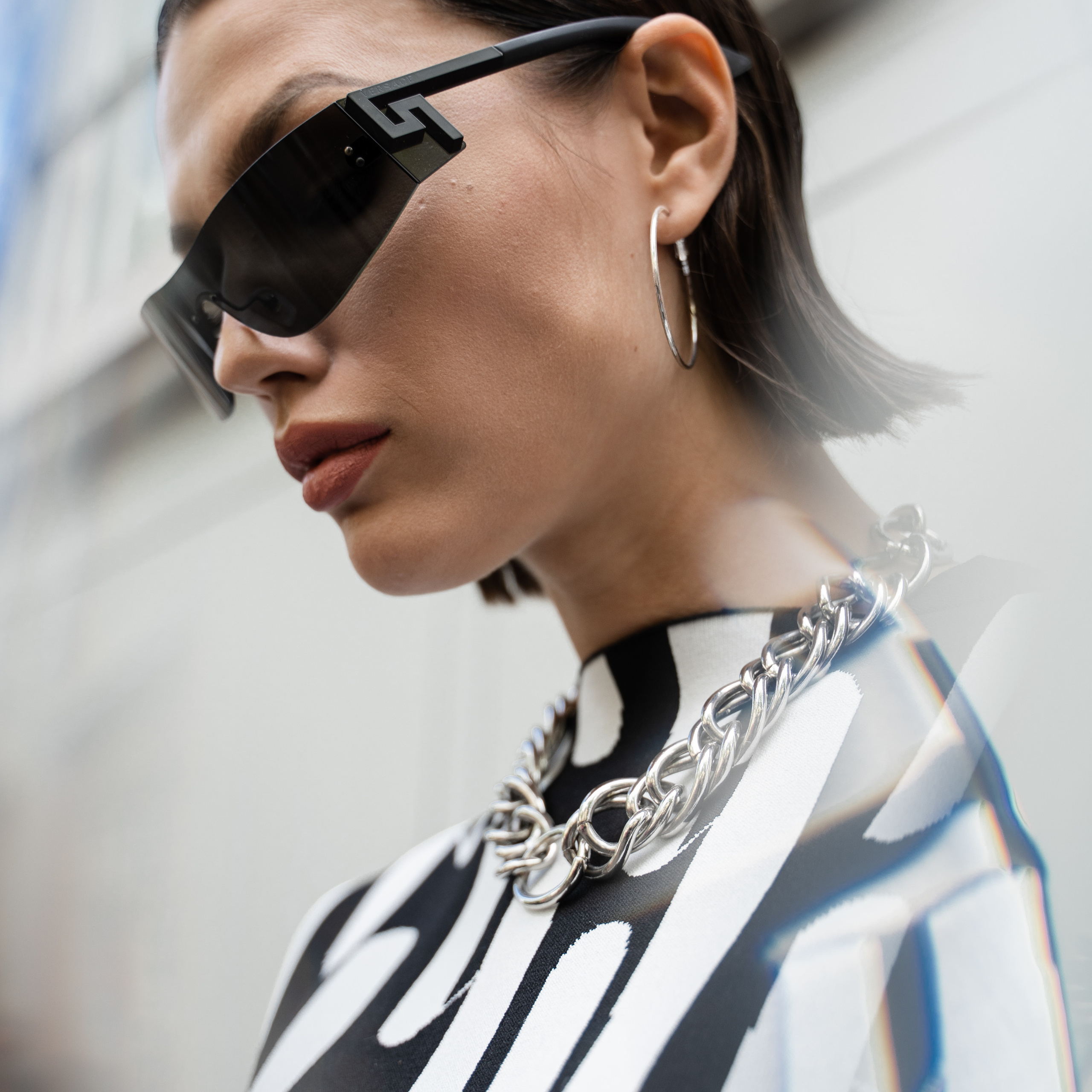 Portrait of a woman wearing dark sunglasses and a silver chain necklace reflecting city lights