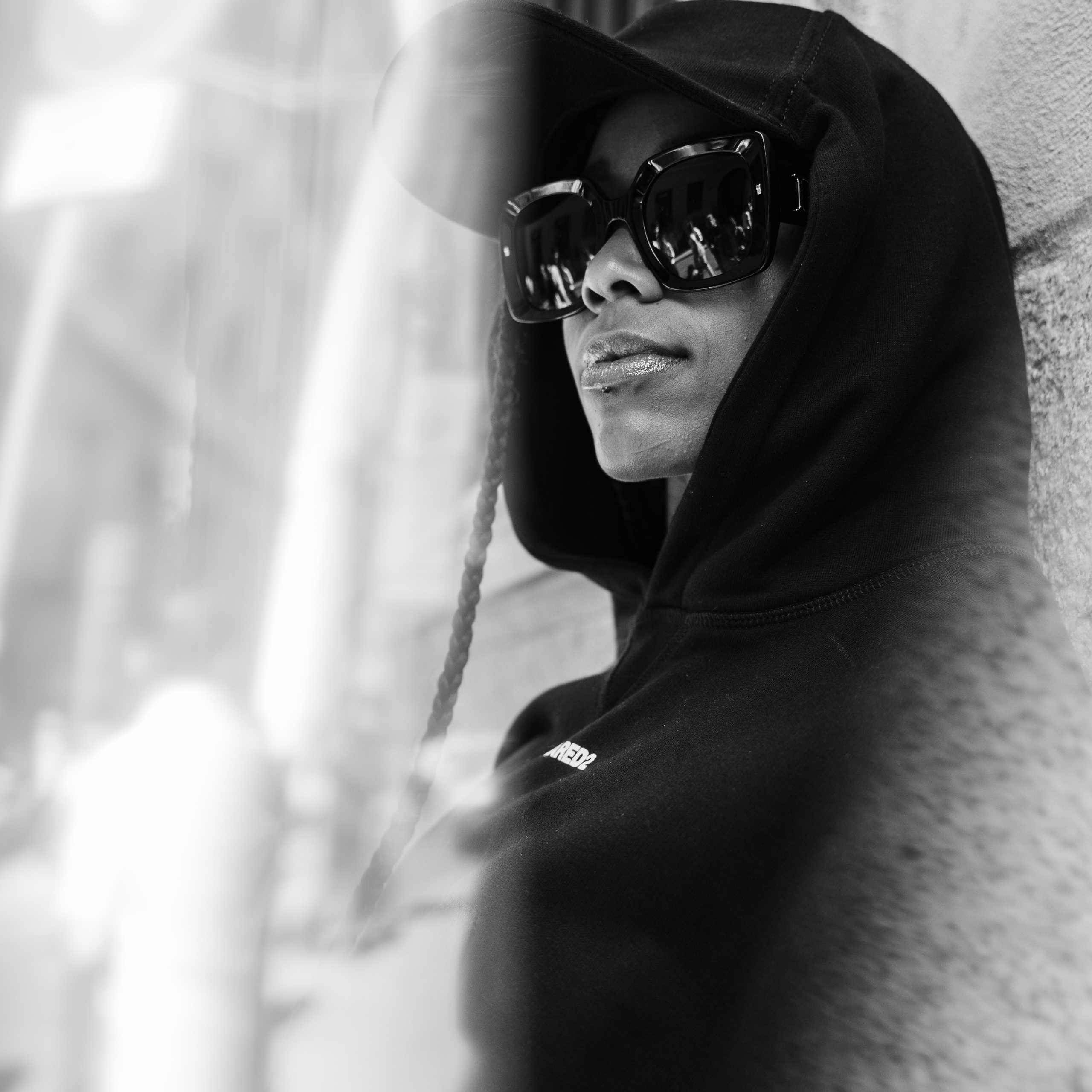 Woman in a black hoodie and oversized sunglasses reflecting the city surroundings, captured in black and white