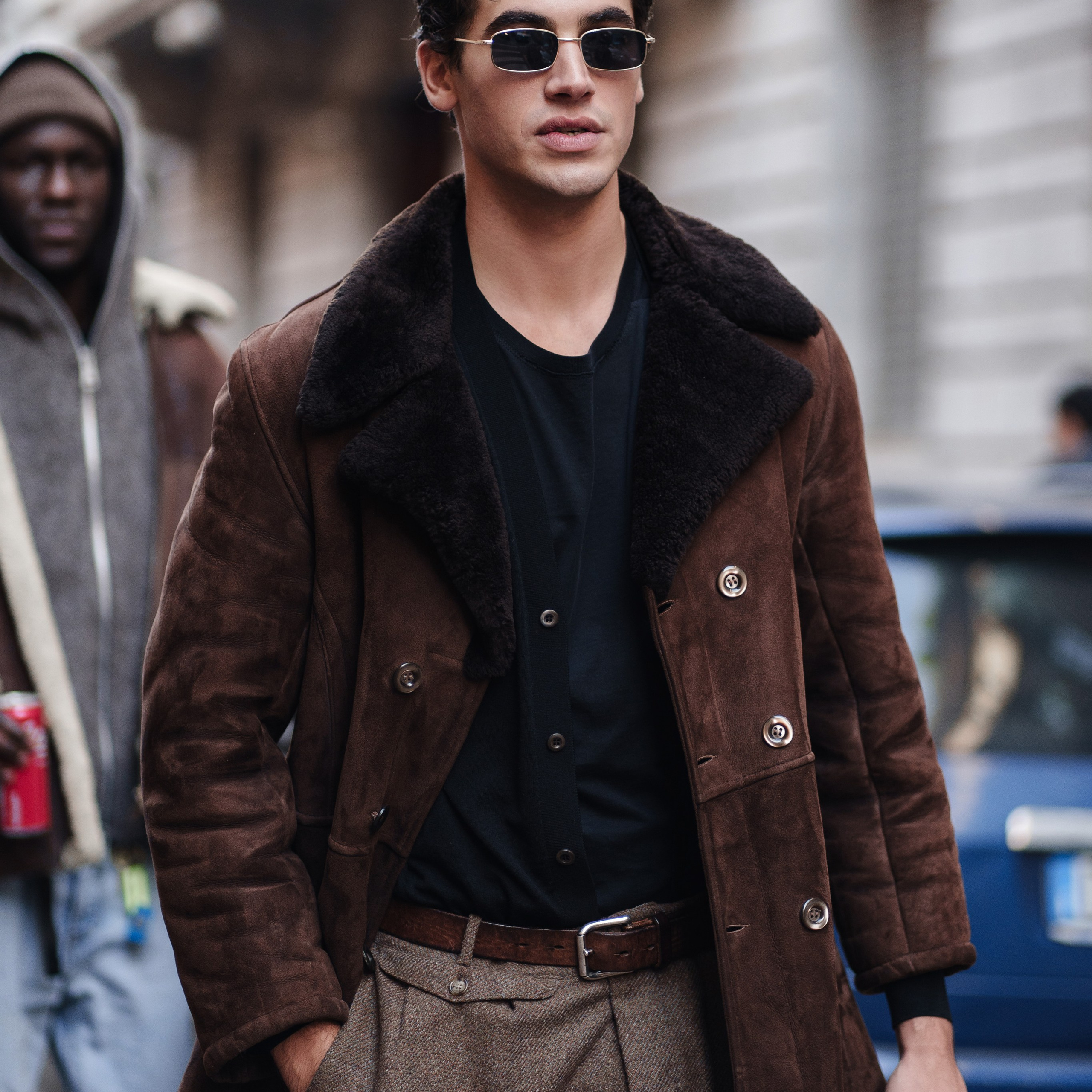 Trendy young man in sunglasses and a brown shearling coat at Milan Fashion Week
