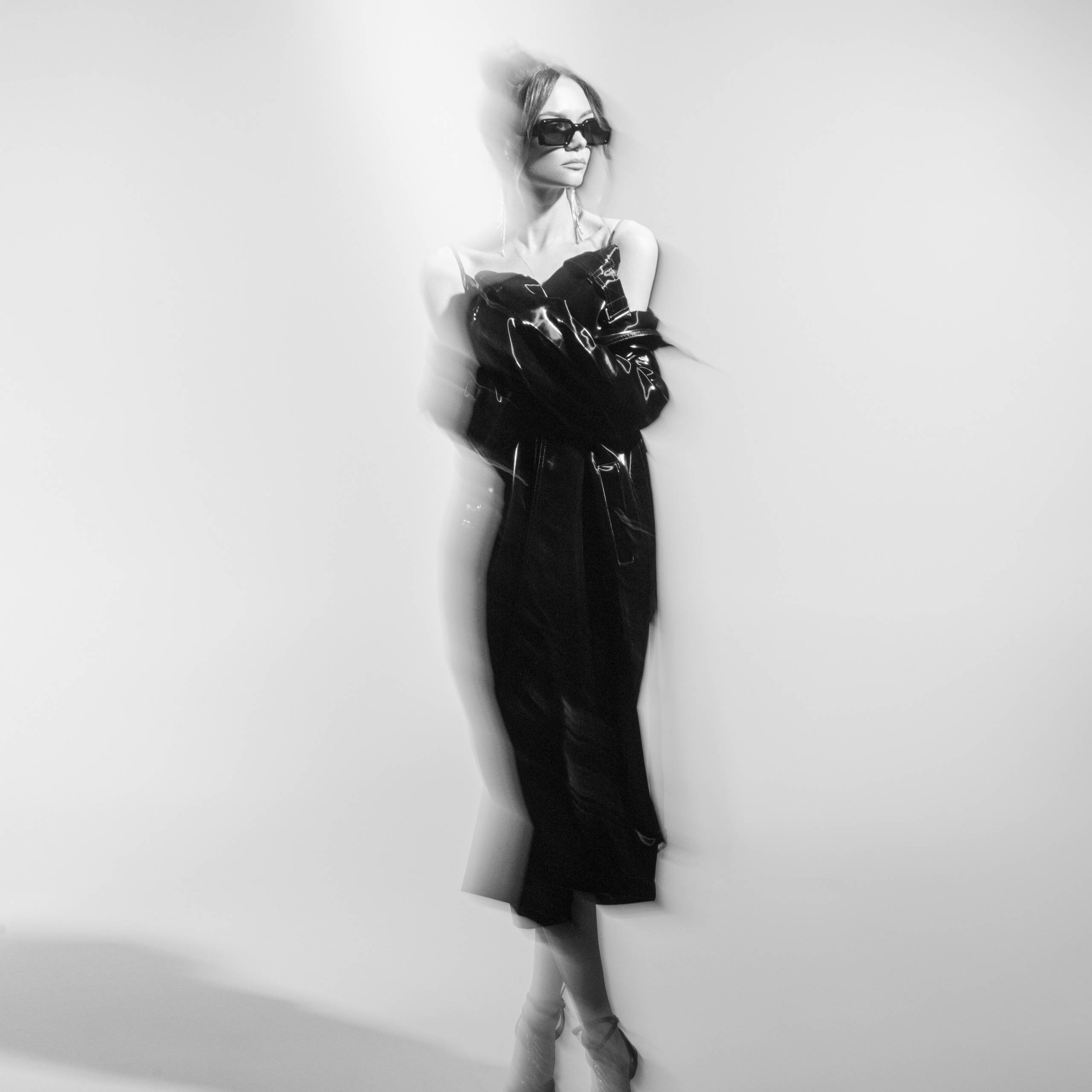 Fashion-forward model in a long black dress and sunglasses posing in a dynamic, blurred motion shot