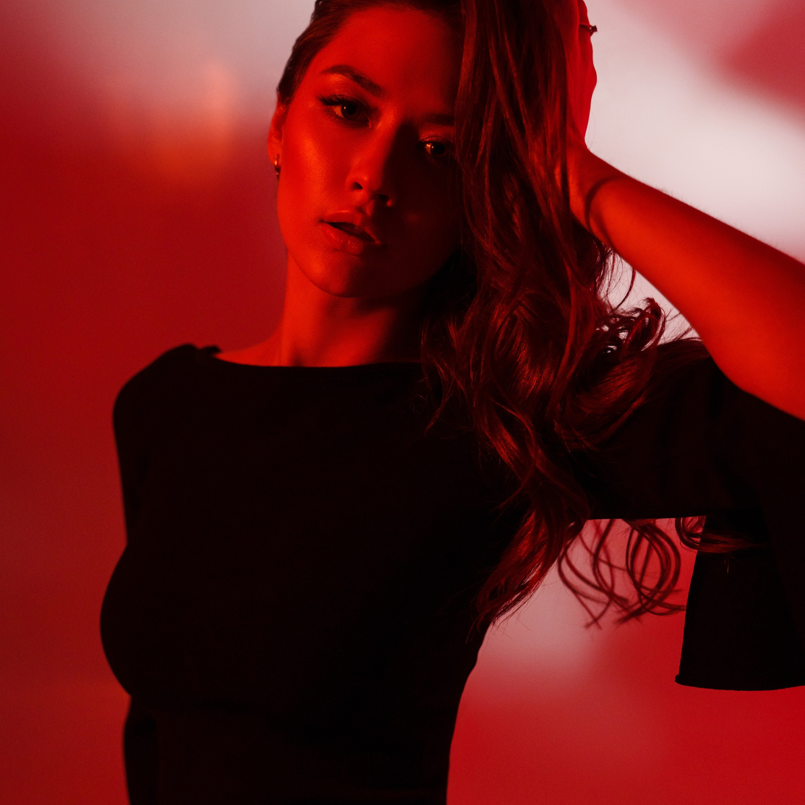 Glamorous portrait of a woman with flowing hair in a black dress, illuminated by red and white dramatic lighting