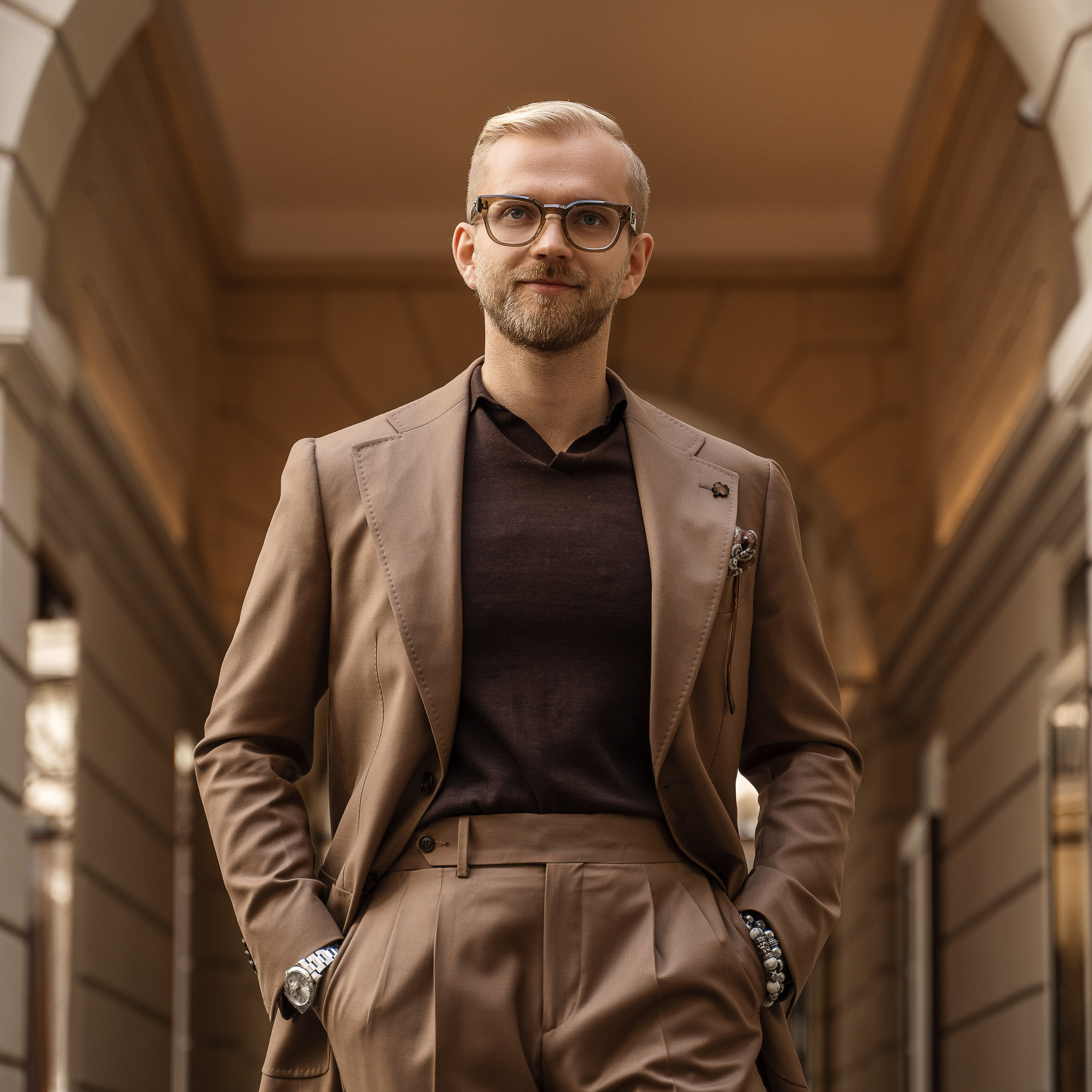 Street style portrait of a stylish man in a brown suit and glasses, posing under an elegant archway in Milan. Fashion photography, portrait photoshoot