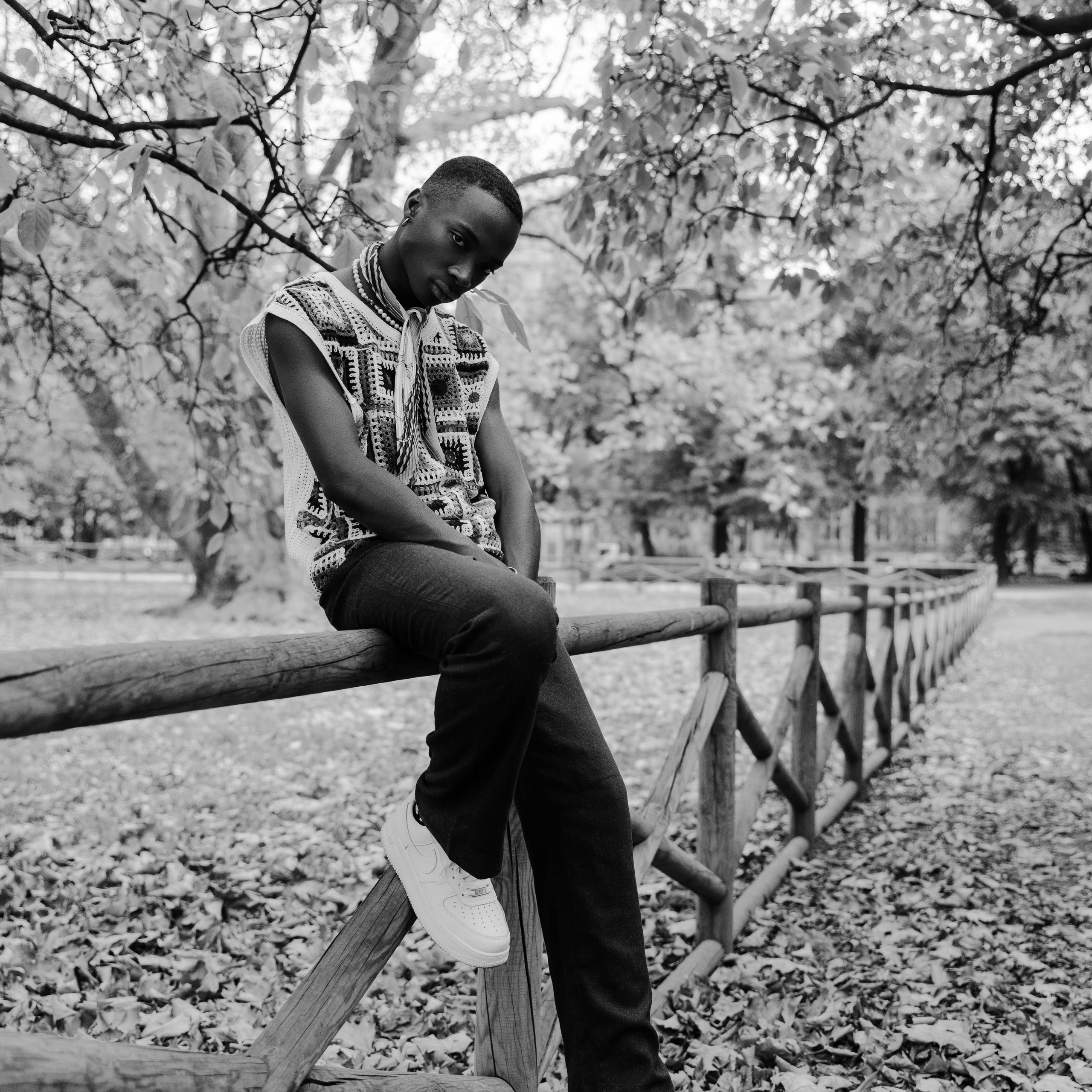 Monochrome image of a young man sitting pensively on a wooden fence in a park