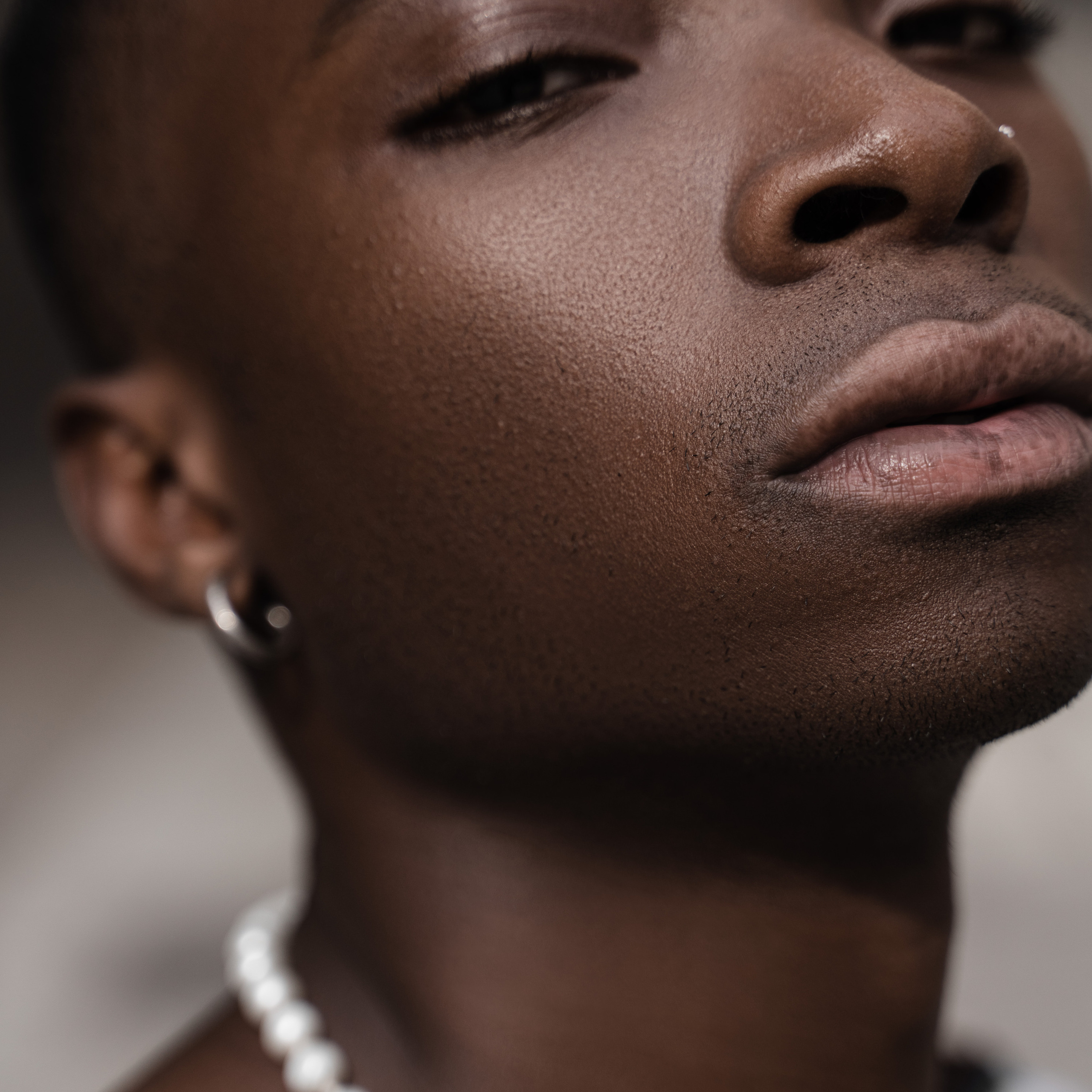 Close-up portrait of a serene young man with pearl necklace and soft-focused background