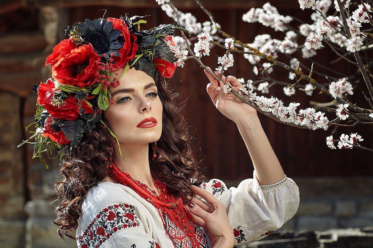 Femme en robe traditionnelle ukrainienne touchant une branche en fleurs – séance photo romantique au printemps