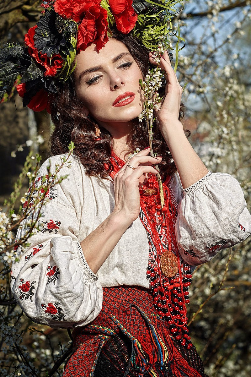 Portrait artistique d'une femme en tenue traditionnelle ukrainienne avec une couronne de fleurs rouges – séance photo folklorique en extérieur