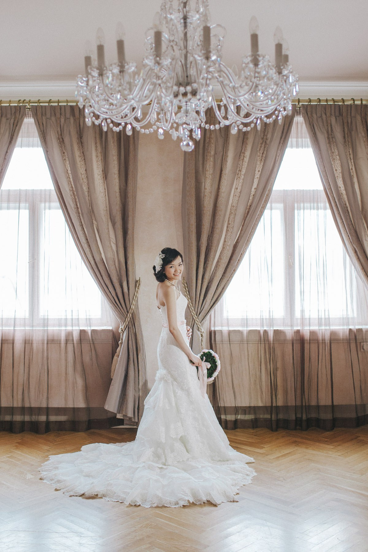 As a large antique chandelier hangs from above, a beautiful Hong Kong bride stands underneath with her bouquet.
