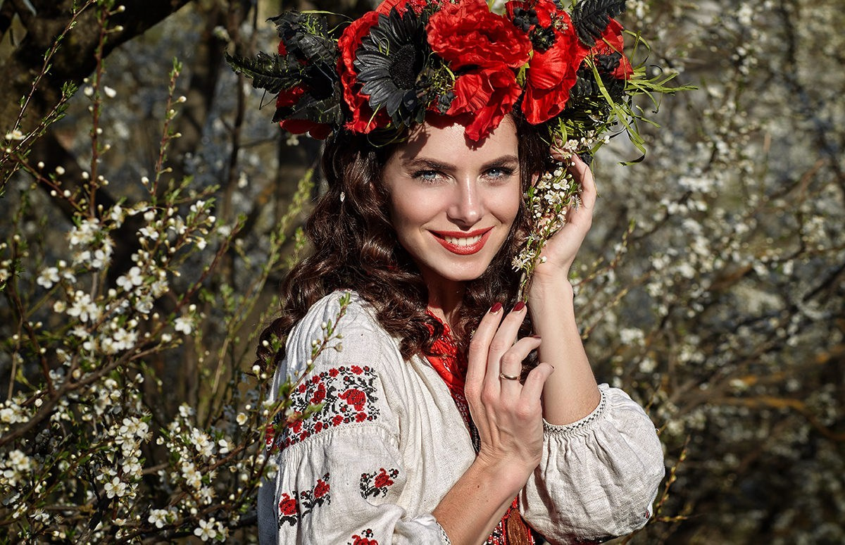 Portrait joyeux d'une femme en costume folklorique ukrainien avec une couronne de fleurs rouges – ambiance chaleureuse et authentique