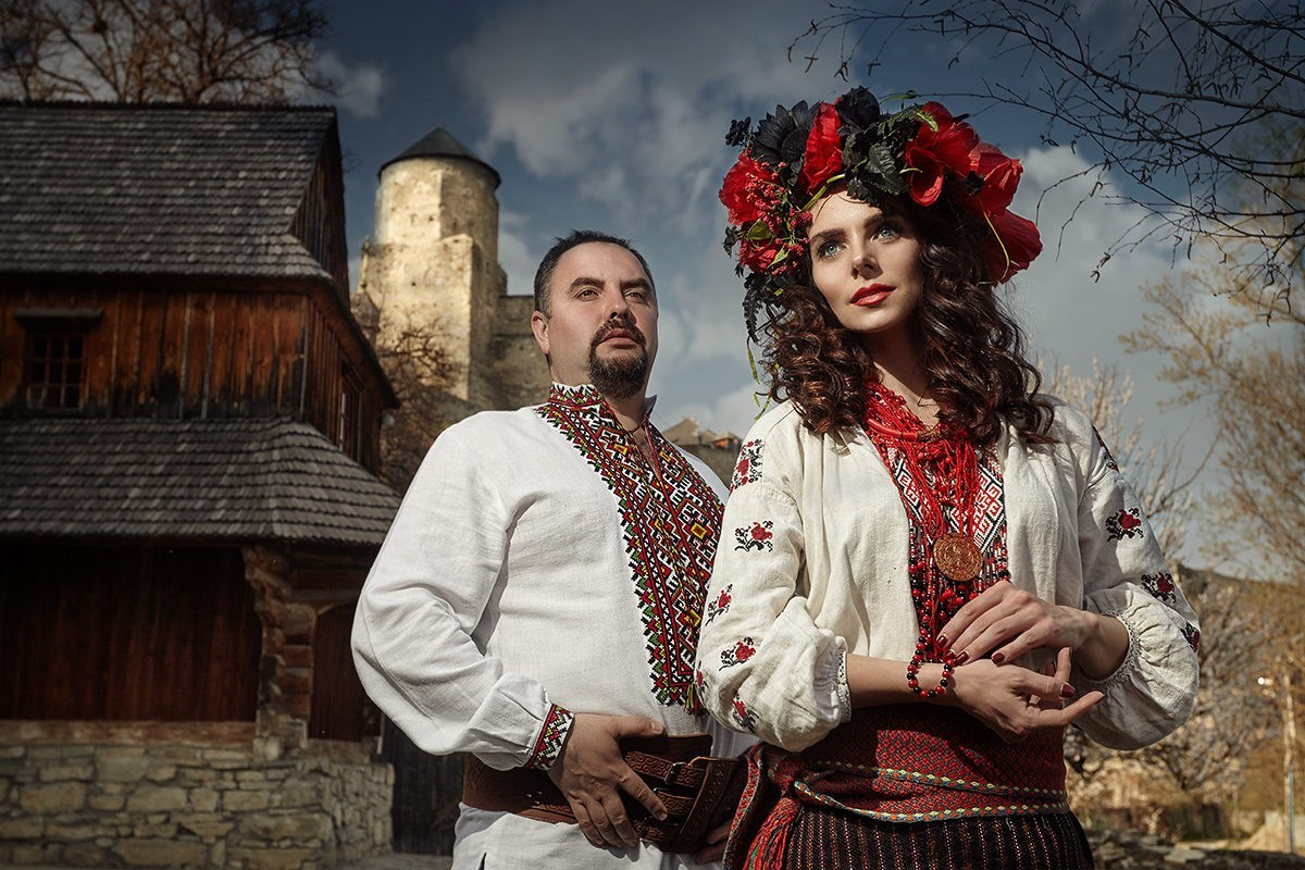 Couple en costumes traditionnels ukrainiens devant une maison en bois – séance photo ethnique avec ambiance historique