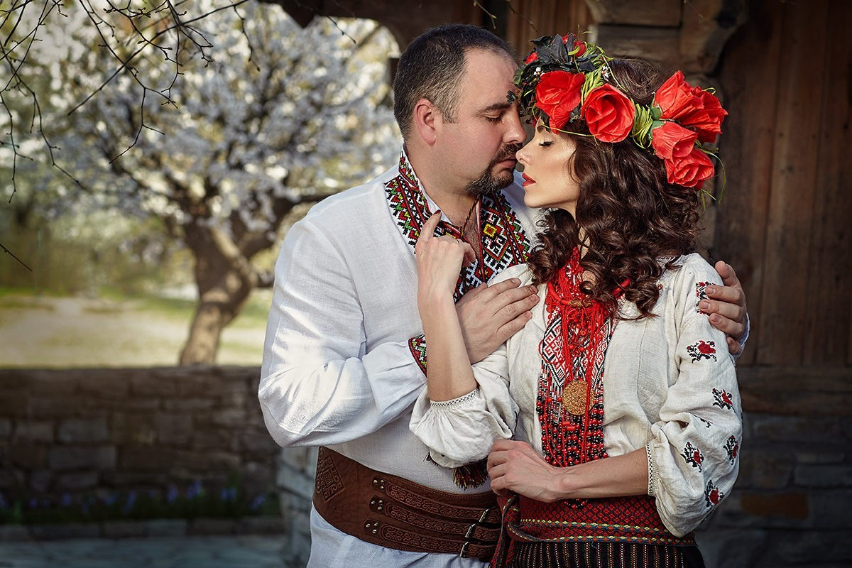 Séance photo de couple amoureux en habits traditionnels ukrainiens – moment tendre au printemps sous les arbres en fleurs