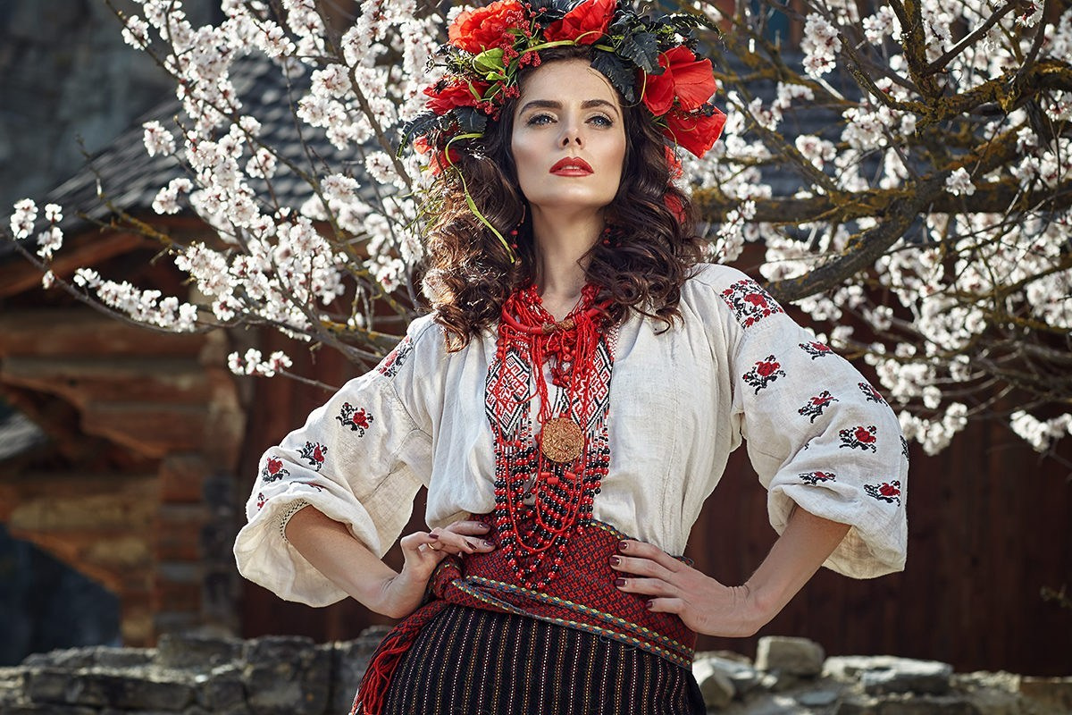 Femme en costume folklorique ukrainien posant fièrement devant un arbre en fleurs – portrait artistique traditionnel au printemps