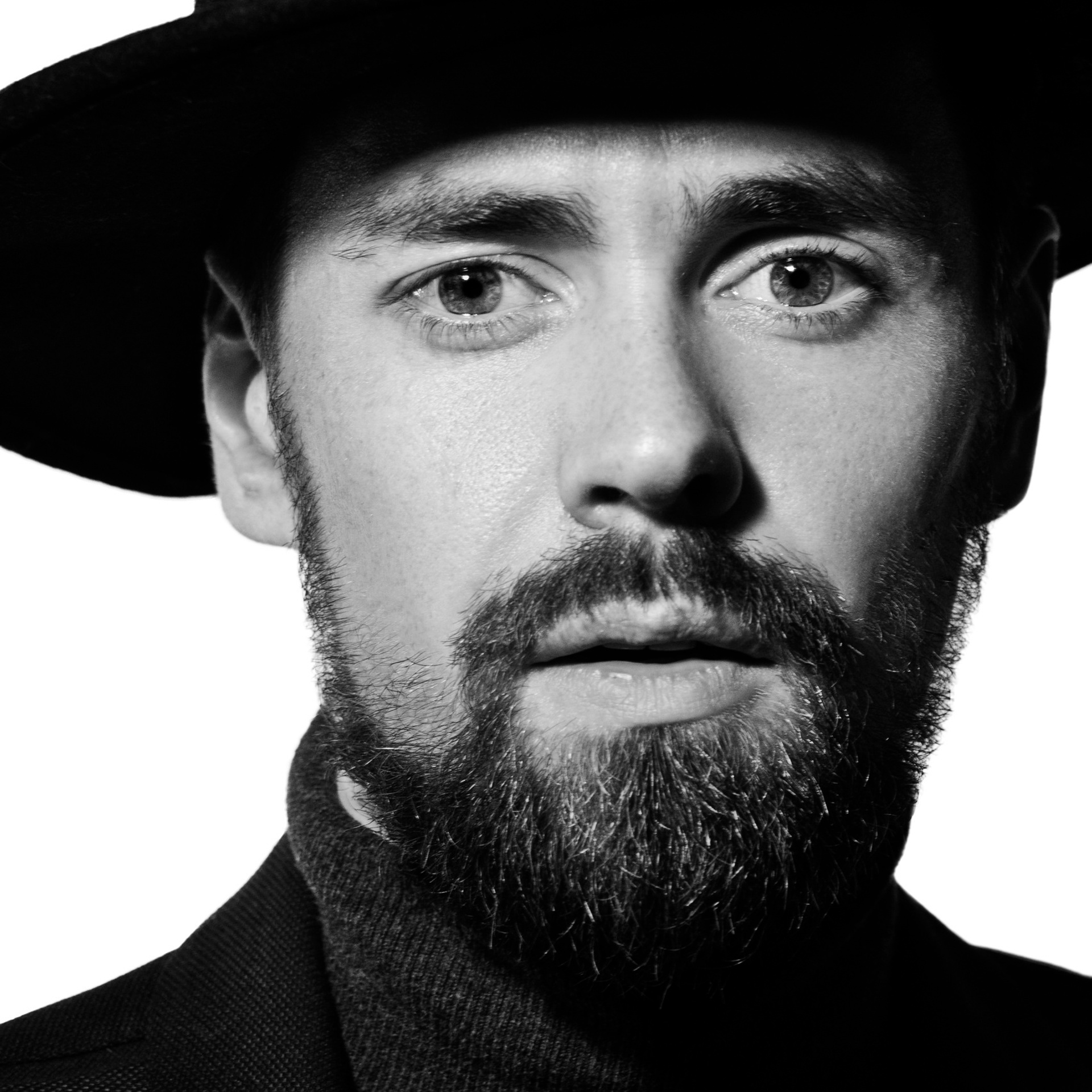 Black and white portrait of a man with a beard wearing a hat and a turtleneck sweater