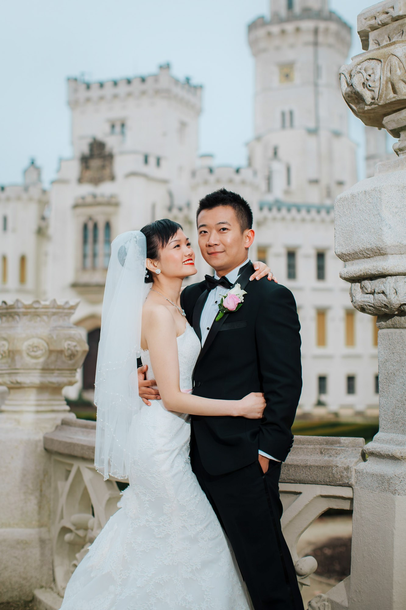 A smilng groom holds his radiant Hong Kong bride as they pose for a portrait on the grounds of the State Chateau of Hluboka during their Czechia destination wedding.