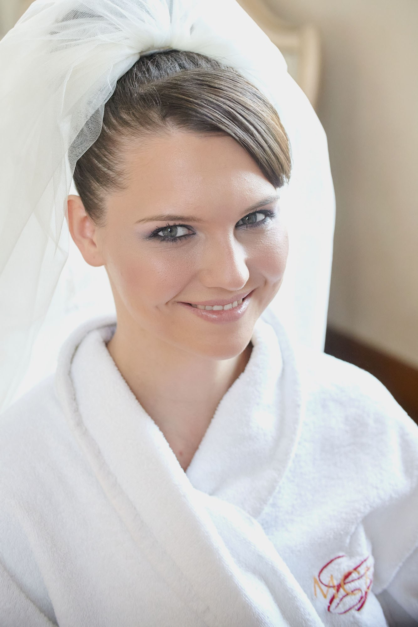Radiant brown-haired bride smiling during wedding prep at a historic chateau.