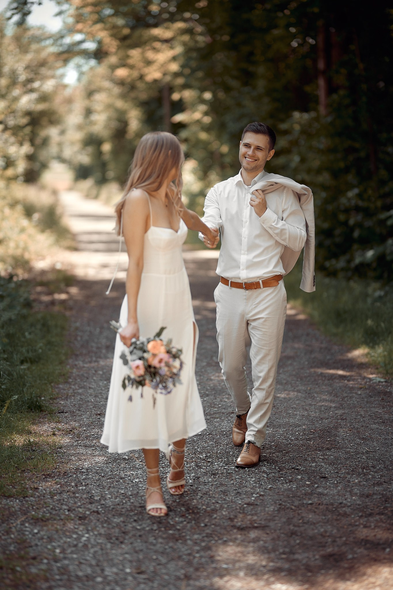 Hochzeitsfotograf Bad Saulgau – romantisches Spaziergangsbild von Sabrina & Max im Wildpark mit Sommerlicht und Brautstrauß