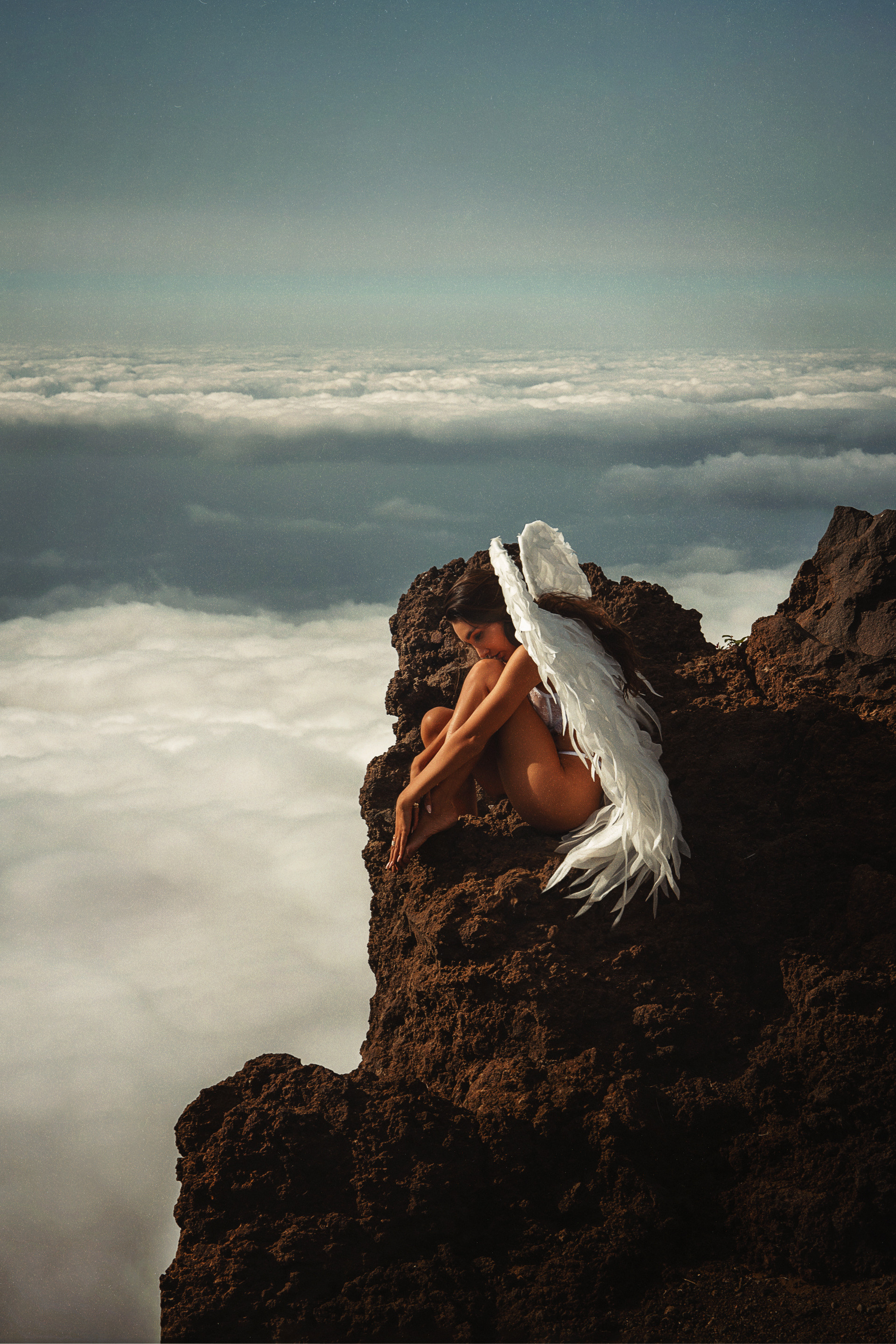 A pretty girl with white wings sitting over the sea of clouds