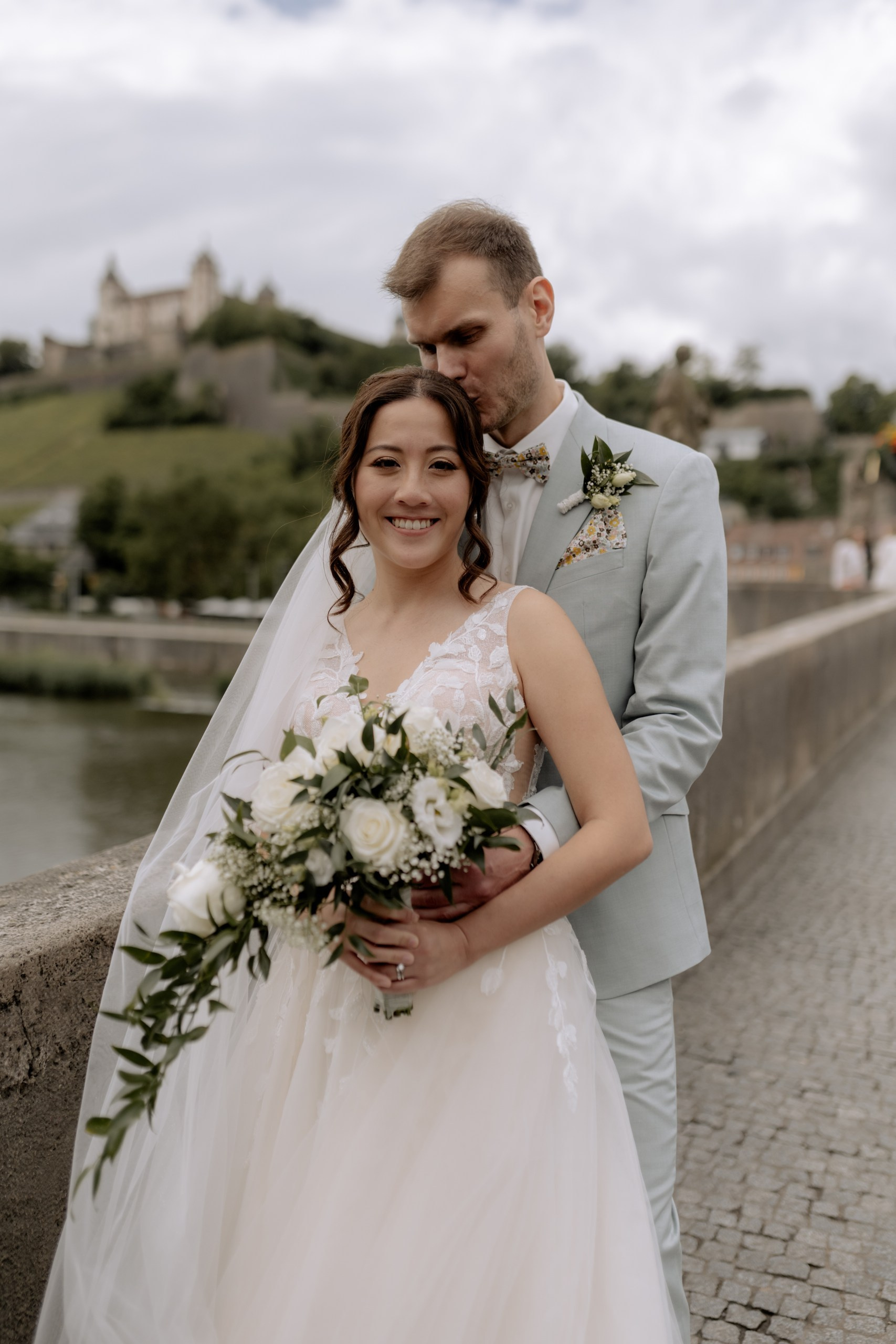 omantischer Moment: Das Paar bleibt mitten auf der Brücke stehen und küsst sich zärtlich, umgeben von historischen Brückenfiguren und vorbeischlendernden Menschen.