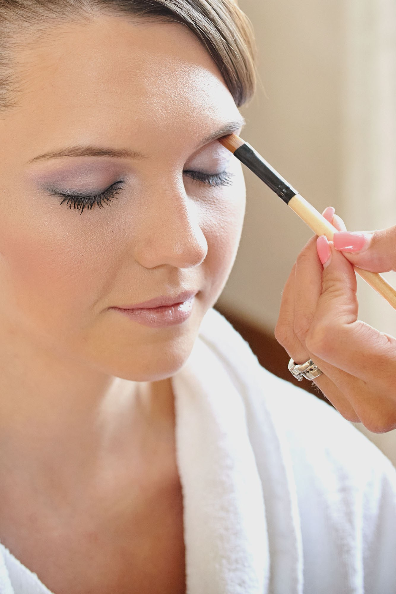 Brown-haired bride receiving eyeliner application during bridal prep.